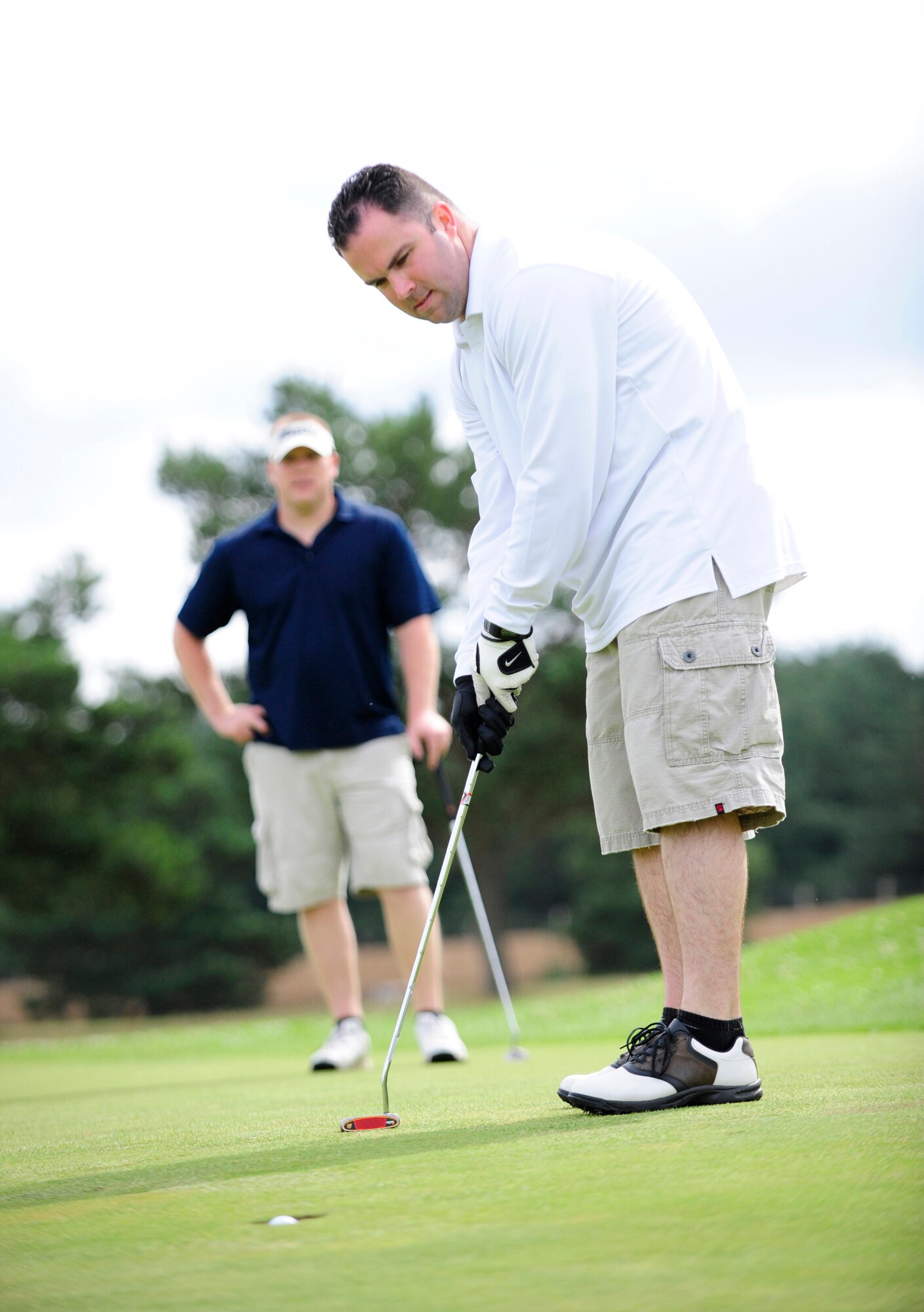 RAF MILDENHALL, England -- Jonathan Barnes, 100th Maintenance Squadron, sinks a birdie putt on the 11th green with playing partner Brian Szarek looking on during the RAF Mildenhall Intramural Golf play-offs at Breckland Pines Golf Club, RAF Lakenheath, July 12, 2011. The birdie gave his team a two-hole lead on the back nine against the 100th Communications Squadron. (U.S. Air Force photo/Senior Airman Ethan Morgan)