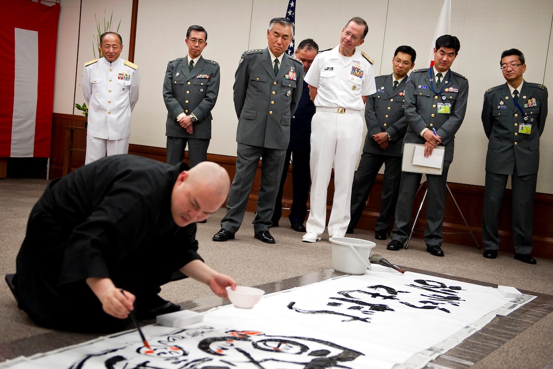 Japanese Gen. Ryoichi Oriki, chief of staff, Japanese Self-Defense Force and U.S. Navy Adm. Mike Mullen, chairman of the Joint Chiefs of Staff, watch Japanese calligraphist Taisan Tanaka create Mullen's name in a "name poem" at the Ministry of Defense in Tokyo, July 15, 2011. The ministry offered the calligraphic character poem as thanks for Mullen's 43 years of service and friendship to Japan and its people.