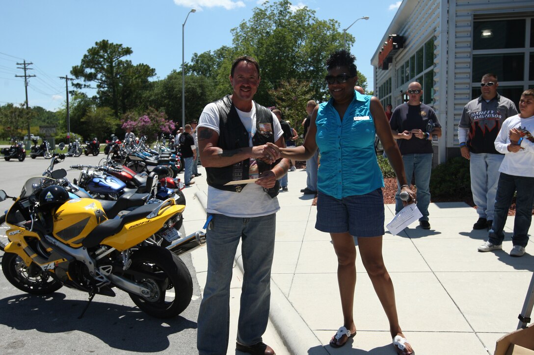 Joe Knipe, a former Marine, and Barbara Robinson, program director with Armed Services YMCA, shake hands during the first Poker Run hosted by the Armed Services YMCA fundraising event at the New River Harley Davidson Buell motorcycle shop in Jacksonville, N.C., July 16. Knipe won the grand prize with a three-of-a-kind of jacks and received a $200 gift certificate from a local tattoo parlor.