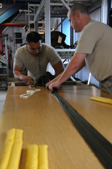 Staff Sgt. Brian Sommers and Tech. Sgt. Phil Shelton, aerial porters with 193rd Special Operations Wing, Middletown, Pa. before packing a parachute, make sure that the parachute lines are straight, so it will deploy. On Jun. 11 they prepared 25-pound parachutes to  be attached to a Container Delivery System used for airdrop training.  (Photo by Air Force Tech. Sgt. Culeen Shaffer)