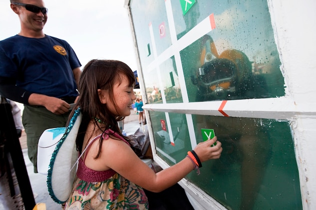 Eight-year-old Zoie Driver, from Honolulu, plays tic-tac-toe with submerged Petty Officer 2nd Class Jason Balavram, a Navy diver with Mobile Dive Salvage Unit One, during BayFest 2011 on Marine Corps Base Hawaii, July 16, 2011. Celebrating its 22nd year as Hawaii’s largest summer music festival, the three-day event — sponsored by Marine Corps Community Services — opened the base’s gates to the local community, featuring concerts by Cecilio and Kapono, Hoobastank, Puddle of Mudd and Joe Nichols, in addition to contests, carnival rides, food booths and military static displays.