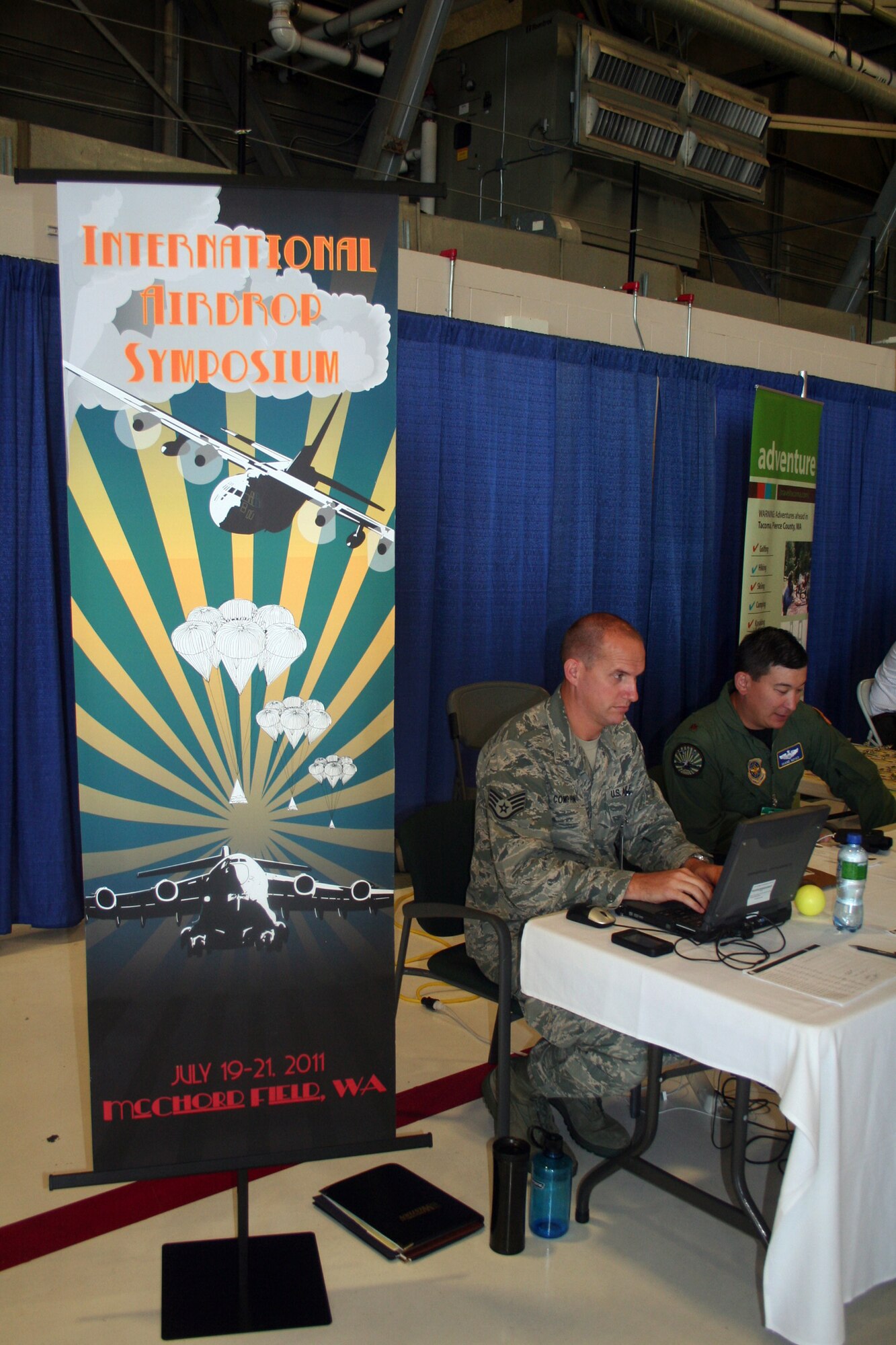 Staff Sgt. Owen Compton and Maj. Shane Noyes, both from Air Mobility Command's Detachment 5 at St. Joseph, Mo., work with participants arriving for the 2011 International Airdrop Symposium inside a hangar at Joint Base Lewis-McChord, Wash., on July 17, 2011. (U.S. Air Force Photo/Master Sgt. Scott T. Sturkol)