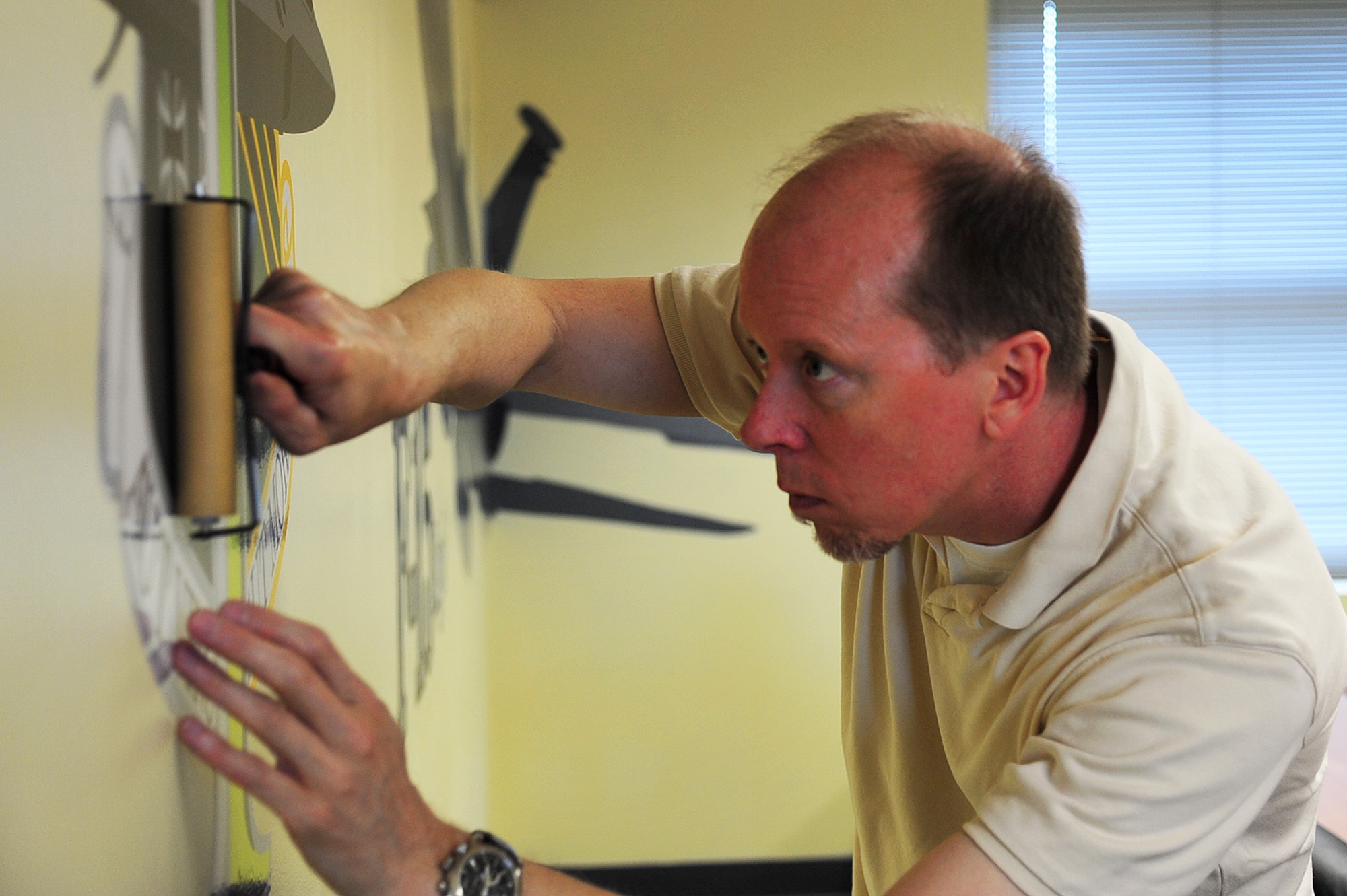 Rodney Adams, Air Combat Command Graphics visual information specialist, adds the 1st Fighter Wing emblem to the F-22 Raptor mural in the Airmen Leadership School Eagle flight classroom at Langley Air Force Base, Va., July 15, 2011. The mural includes an F-15 Eagle, an F-22 Raptor, the 1st Fighter Wing emblem and wallpaper border. (U.S. Air Force photo by Airman 1st Class Camilla Griffin/Released)