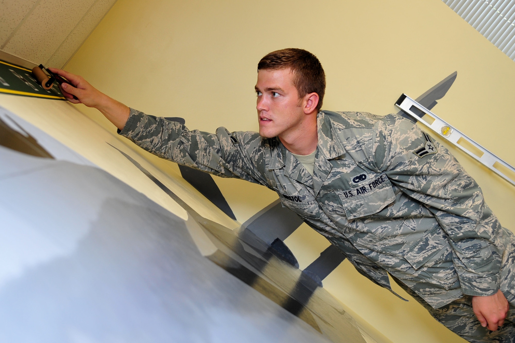 Airman 1st Class Jacob Bristol, 1st Maintenance Squadron precision guided missile technician, places a 1st Fighter Wing wallpaper border in the Airmen Leadership School Eagle flight classroom at Langley Air Force Base, Va., July 15, 2011. Members of the 1st FW spent a week renovating and painting an F-22 Raptor mural in the classroom to preserve 1st FW heritage. (U.S. Air Force photo by Airman 1st Class Camilla Griffin/Released)