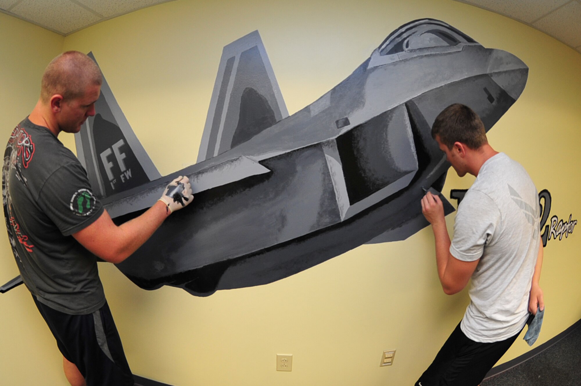 Airmen 1st Class Jacob Bristol and Shane McNaughton, 1st Maintenance Squadron precision guided missile technicians, add minor details to an F-22 Raptor mural at Langley Air Force Base, Va., July 13, 2011. Airmen from the 1st Fighter Wing spent a week painting the mural in the Eagle flight classroom at the Airmen Leadership School. (U.S. Air Force photo by Airman 1st Class Camilla Griffin/Released)