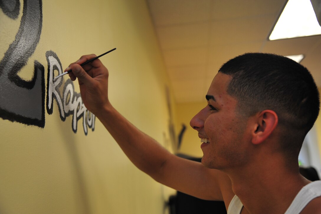 Airman 1st Class Israel Medina, 1st Operations Support Squadron air crew flight equipment technician, fills in lettering on an F-22 Raptor mural at Langley Air Force Base, Va., July 12, 2011. Airmen from the 1st Fighter Wing spent a week painting the mural in the Eagle flight classroom at the Airman Leadership School. (U.S. Air Force photo by Airman 1st Class Camilla Griffin/Released)