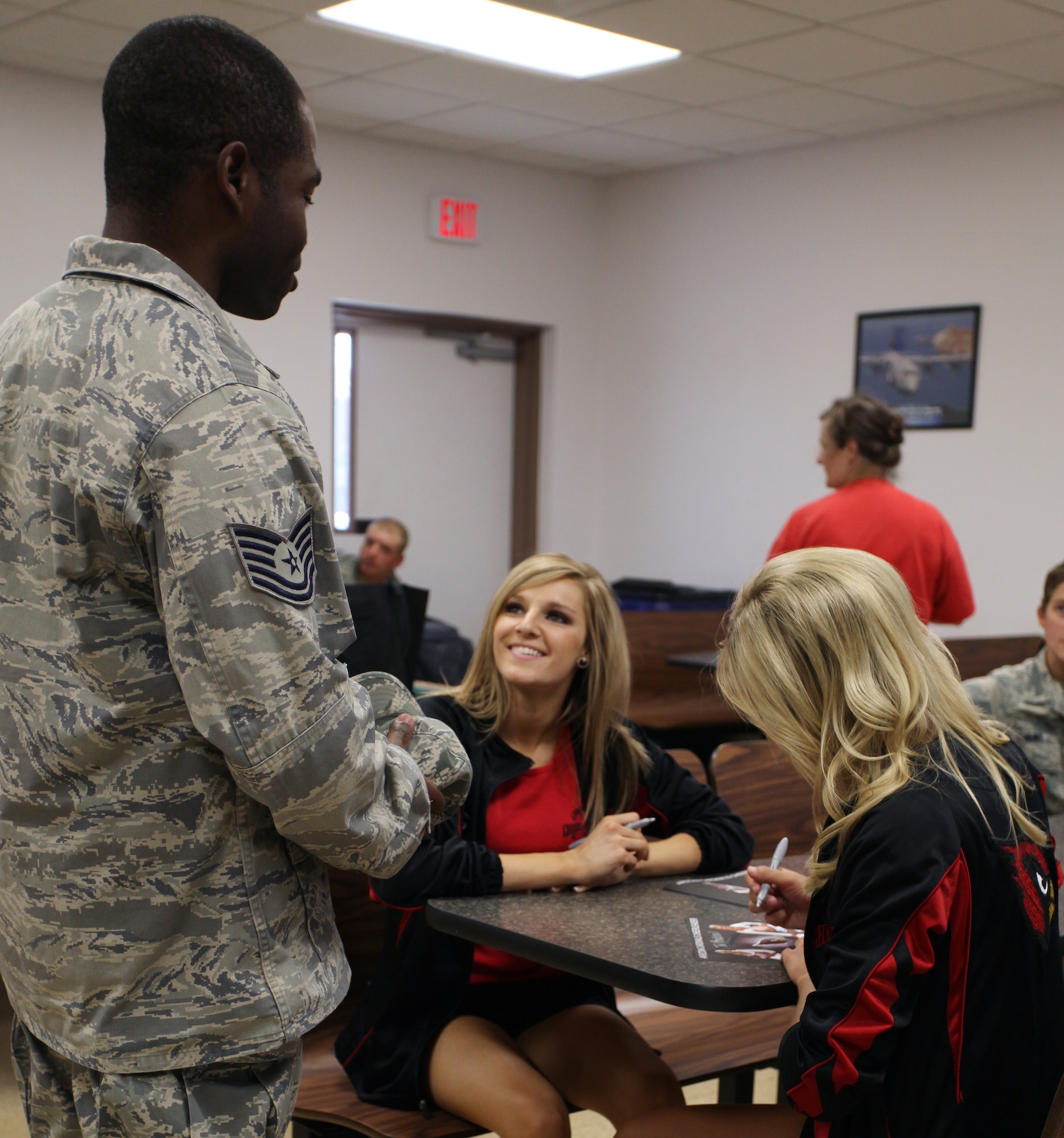 Kimberly Haug and Emily Jones, Arizona Cardinals cheerleaders, autograph a photo for Tech. Sgt. Andrew Wallace, 27th Special Operations Civil Engineer Squadron, during their visit to Cannon Air Force Base, N.M., July 15, 2011.  The cheerleaders toured the base as part of an Army and Air Force Exchange-sponsored morale event.  (U.S. Air Force photo by Airman 1st Class Jette Carr)(RELEASED)
