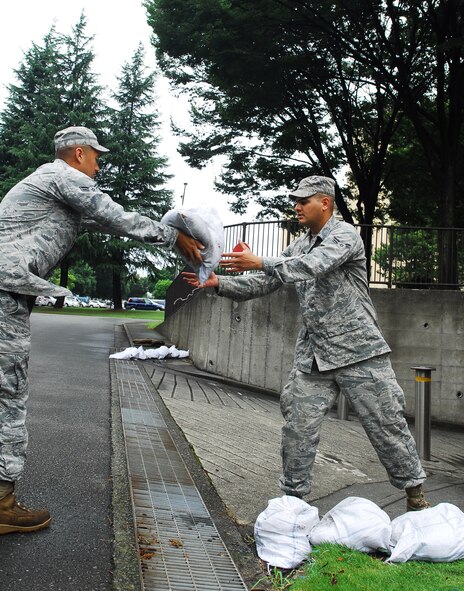YOKOTA AIR BASE, Japan -- Airman 1st Class John Martinez (left), and Airman 1st Class Paul Scheck, both pavement and construction journeymen from the 374th Civil Engineer Squadron horizontal repair flight, work to place sandbags near a storm drain in a residential tower July 20, 2011, at Yokota Air Base, Japan. Personnel from the 374th CES ensured storm damage prevention measures were in place during the recent rainfall received on base as a result of a tropical cyclone located near Japan in the Pacific Ocean. (U.S. Air Force photo/Staff Sgt. Robin Stanchak)