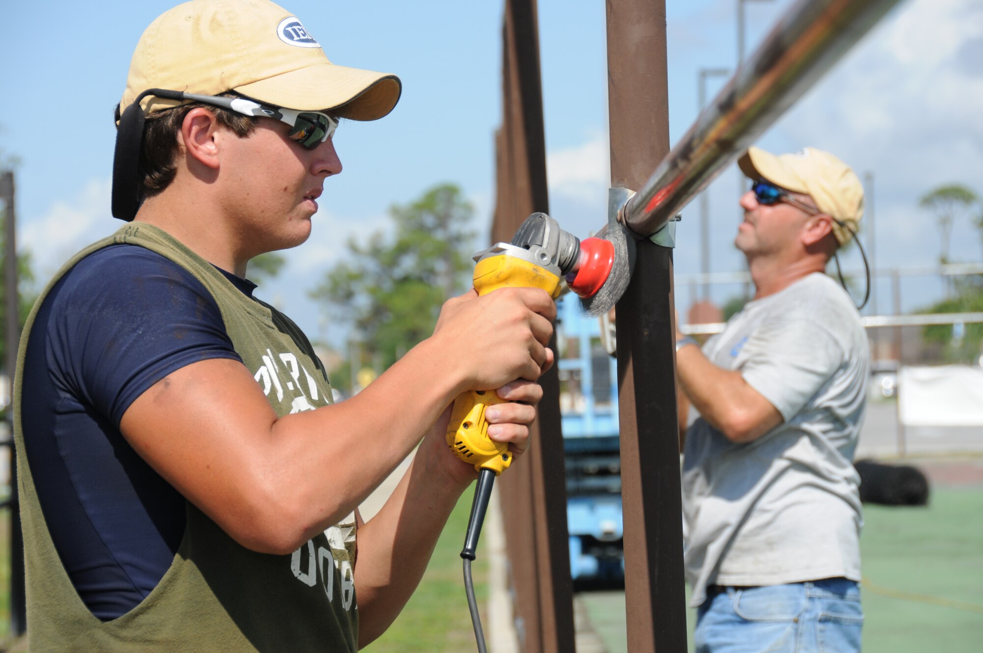 Laborer Zack Bates, left, and project supervisor Billy Spiers from Industrial Environmental Management of Poplarville, Miss., sand the poles surrounding the tennis courts on Meadows Drive for repainting July 19.  (U.S. Air Force photo by Kemberly Groue)