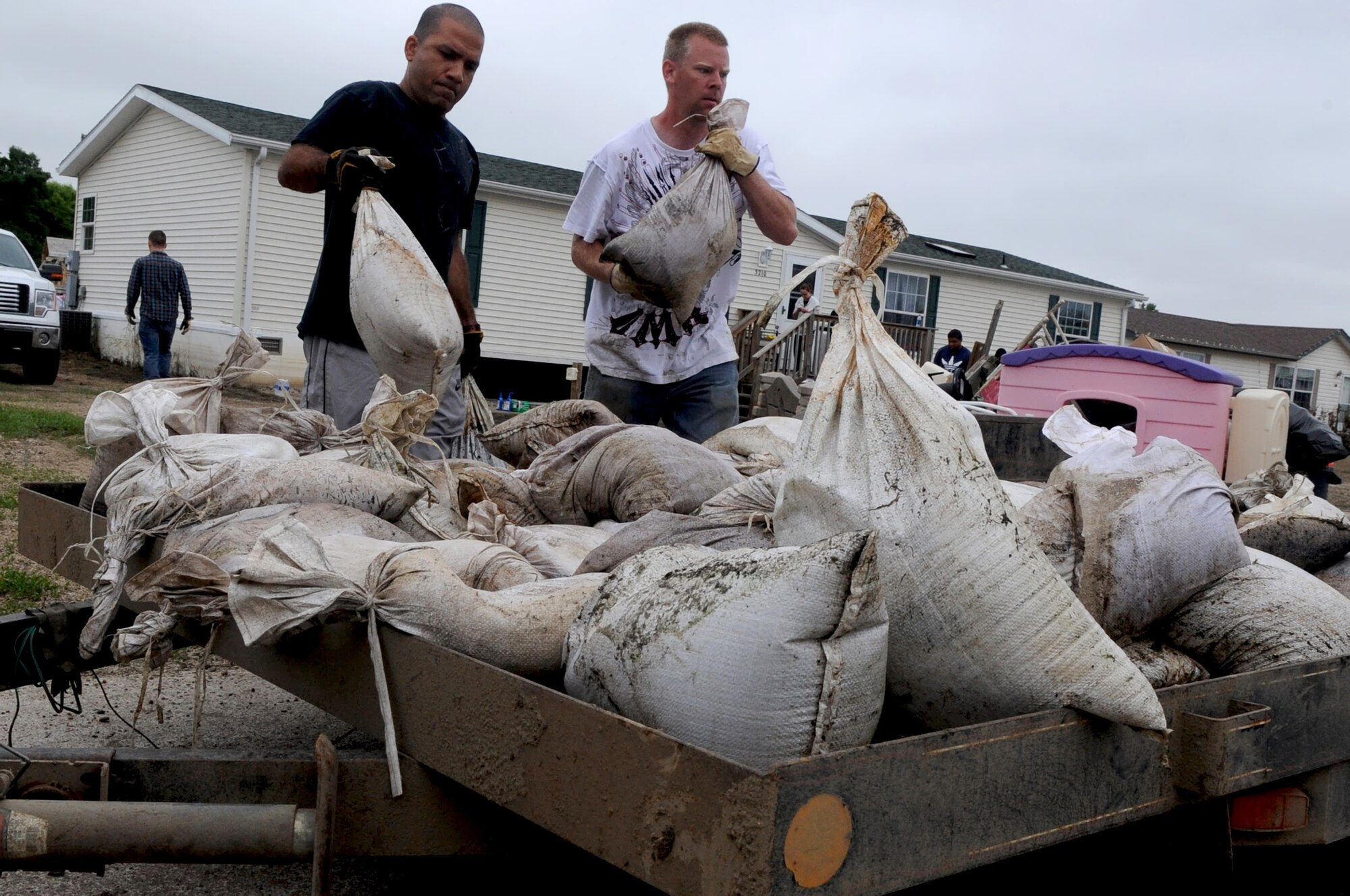 MINOT AIR FORCE BASE, N.D. -- Capt. Eddie Rubero, 5th Bomb Wing chaplain and Tech. Sgt. Lance Berentson, 741st Missile Squadron facility manager, load sandbags onto a trailer July 14. Berentson was one of the more than 1,100 Air Force Global Strike Command Airmen affected by the recent historic flooding situation, but was recently allowed back into his home. However, on arrival, he noticed their basement was flooded, their house’s foundation damaged and their yard in shambles. (U.S. Air Force photo/Airman 1st Class Jose L. Hernandez) 
