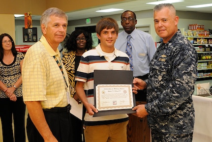 Cmdr. Charles Phillip and Larry Jackson present Bobby O’Brien with a plaque for being one of the winners of the Scholarships for Military Children July 20 at the Joint Base Charleston - Weapons Station commissary. The scholarship, provided by the Defense Commissary Agency, Fisher House Foundation and S & K Sales is awarded on the basis of meritorious achievement in academic studies, citizenship, school and community activities, leadership and a 500 word essay. The Scholarships for Military Children program provides needed educational opportunities to the children of military families. Phillip is the 628th Mission Support Group executive officer. Jackson is from S & K sales. (Mass Communication Specialist 3rd Class Brannon Deugan)