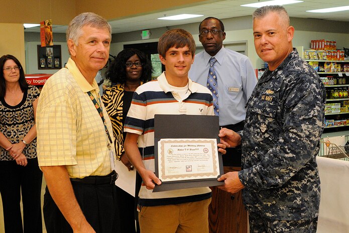 Cmdr. Charles Phillip and Larry Jackson present Bobby O’Brien with a plaque for being one of the winners of the Scholarships for Military Children July 20 at the Joint Base Charleston - Weapons Station commissary. The scholarship, provided by the Defense Commissary Agency, Fisher House Foundation and S & K Sales is awarded on the basis of meritorious achievement in academic studies, citizenship, school and community activities, leadership and a 500 word essay. The Scholarships for Military Children program provides needed educational opportunities to the children of military families. Phillip is the 628th Mission Support Group executive officer. Jackson is from S & K sales. (Mass Communication Specialist 3rd Class Brannon Deugan)