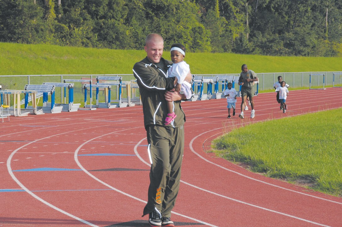 Lance Cpl. Cody Johnson carries a toddler around the track during Kids on the Move at Albany State University, July 22. Roughly 10 children, close to her age, tested their endurance during the event.
