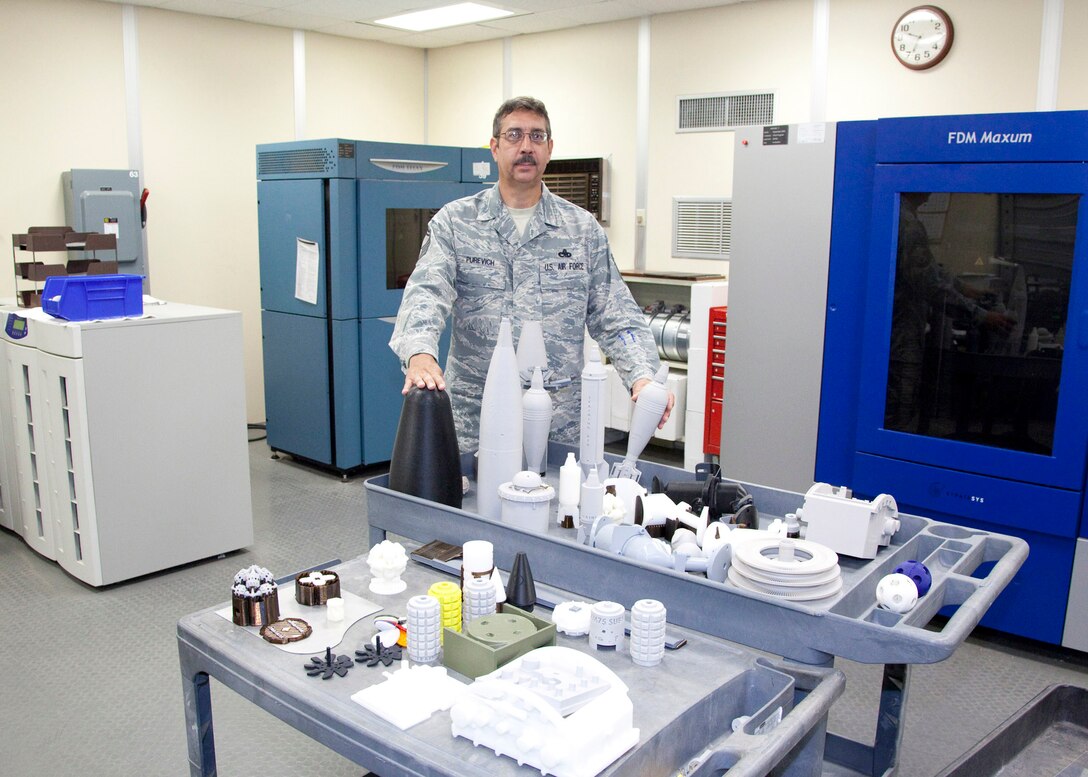 Senior Master Sgt. Walter Purevich of the 982d Maintenance Squadron shows the different types of training devices that the 3D Fused Deposition Modeling makes July 22.The machine creates Explosive Ordinance Disposal training devices, safe for instructional training, Aircraft Models for the F-16, MQ-1, MQ-9, satellite and medical training aids. (U.S. Air Force photo/Danny Webb)