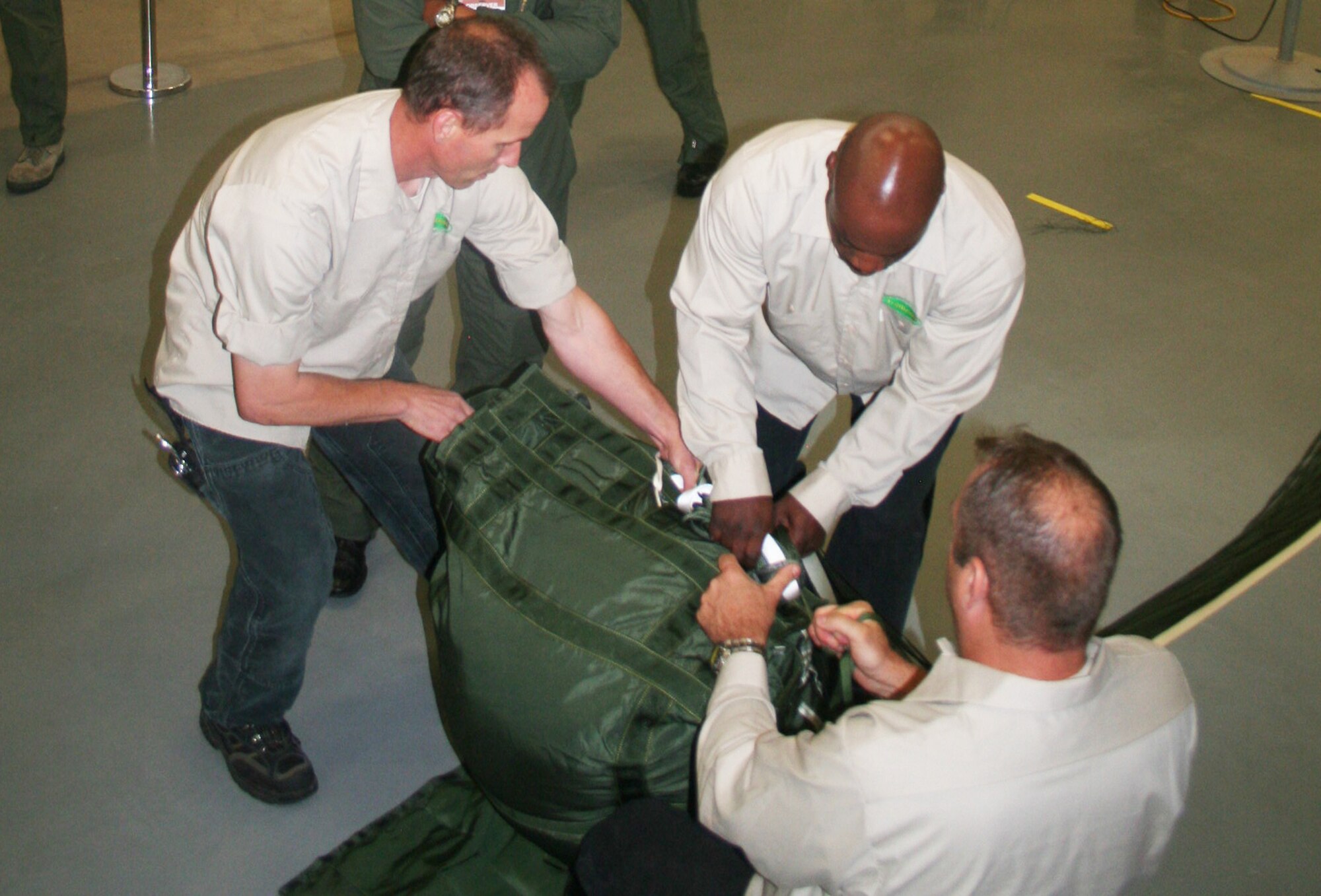Jay Boison, Romereo Scruggs and Allan Lebleu, parachute riggers at the 62nd Aerial Port Squadron aerial delivery facility, prepare a parachute for an airdrop bundle during operations at the facility July 21, 2011, at Joint Base Lewis-McChord, Wash. Boison, Scruggs, and Lebleu, who work for contractor Trailboss, Inc., are among eight people who operate the facility and prepare airdrop training bundles for the 62nd Airlift Wing's mission. (U.S. Air Force Photo/Master Sgt. Scott T. Sturkol)