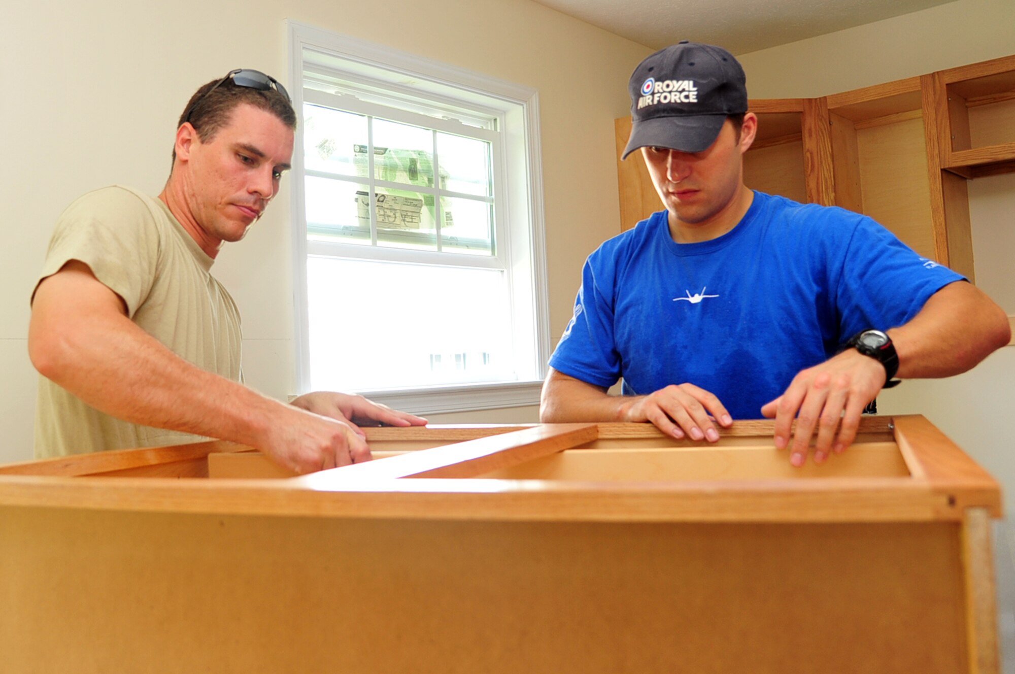 Capt. Travis Passey, and Royal Air Force Flight Lt. Johnathan Smith, 94th Fighter squadron F-22 Raptor pilots, put a cabinet together for a Habitat for Humanity project in Newport News, Va., July 21, 2011. Habitat for Humanity seeks volunteers, like Airmen from the 1st Fighter Wing, to build and rehabilitate houses. (U.S. Air Force photo by Airman 1st Class Camilla Griffin/Released)
