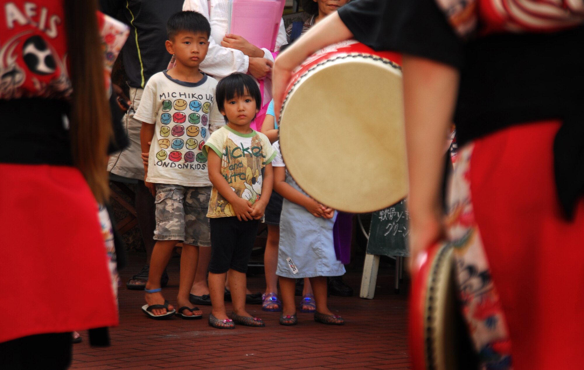 Children watch as students from Amelia Earhart Intermediate School on Kadena Air Base, Japan, perform Eisa dancing and Taiko drumming for locals, military members and their families in Okinawa City during the kick-off of the Kijimuna Festival on July 23, 2011. This annual, nine-day celebration is designed to showcase performing arts, workshops and other activities to youth. This year's event consists of performing arts companies from 14 countries and is the first time that American children have performed traditional Okinawan dance in this forum. (U.S. Air Force Photo by Tech. Sgt. Jocelyn Rich)