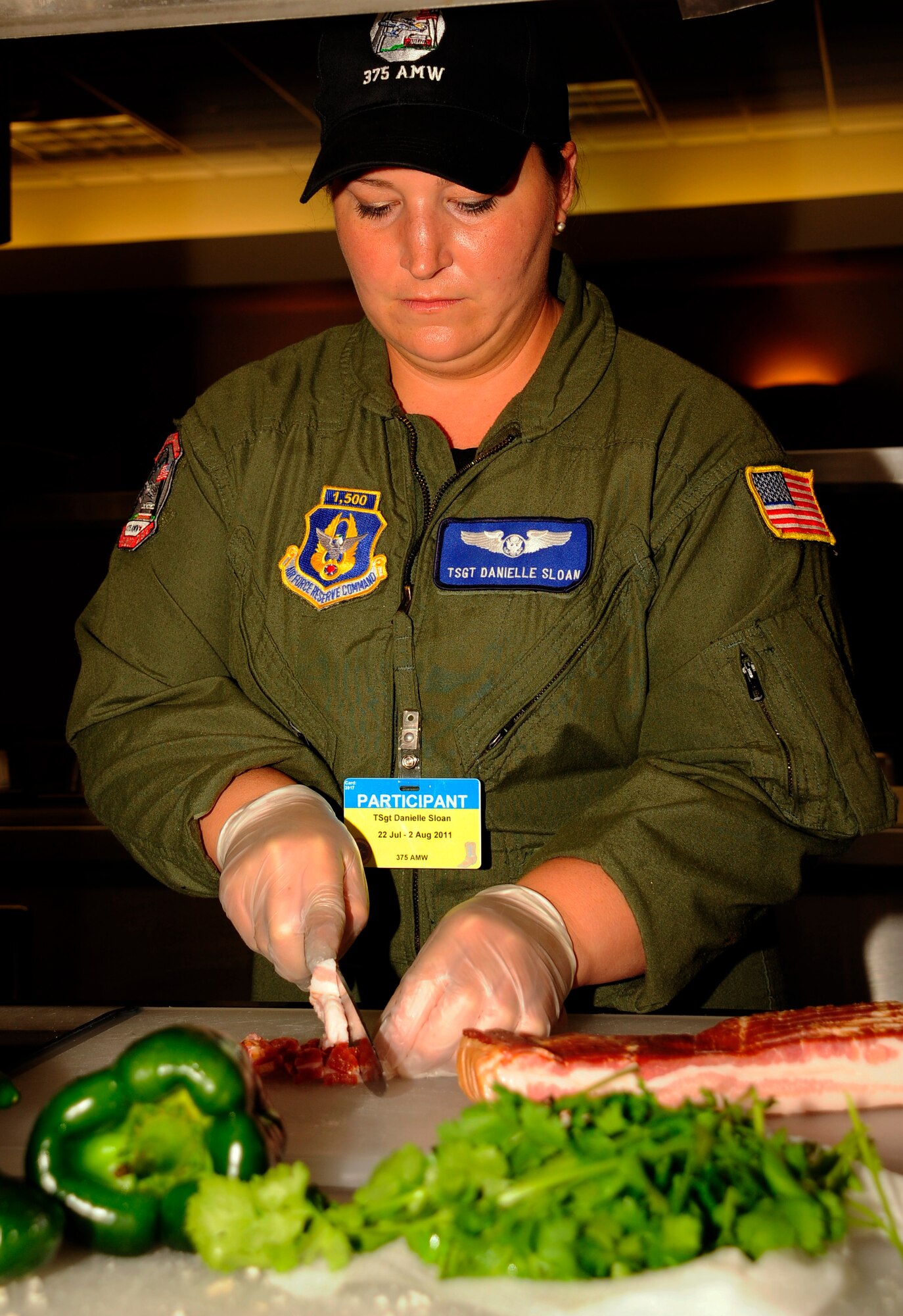 Tech. Sgt. Dani Sloan prepares a slab of bacon, July 25, 2011, as part of the first-ever Air Force flight attendant culinary competetion at Air Mobility Rodeo 2011, Joint Base Lewis-McChord, Wash. The judges, Chief Master Sgt. Seina Enwright (center right) and Staff Sgt. Cat Wilkerson observed the competition to ensure all meals were prepared safely. In addition, the judges rated the meals based on taste, presentation and creativity. Five, two-person teams from around the Air Force competed in the event. The only Total Force team, Sloan, a Reservist, and her teammate, Staff Sgt. Amy Gillilan are from the 73rd and 54th Airlfit Squadrons, Scott Air Force Base, Ill., respectively. (U.S. Air Force photo/Staff Sgt. J.G. Buzanowski)