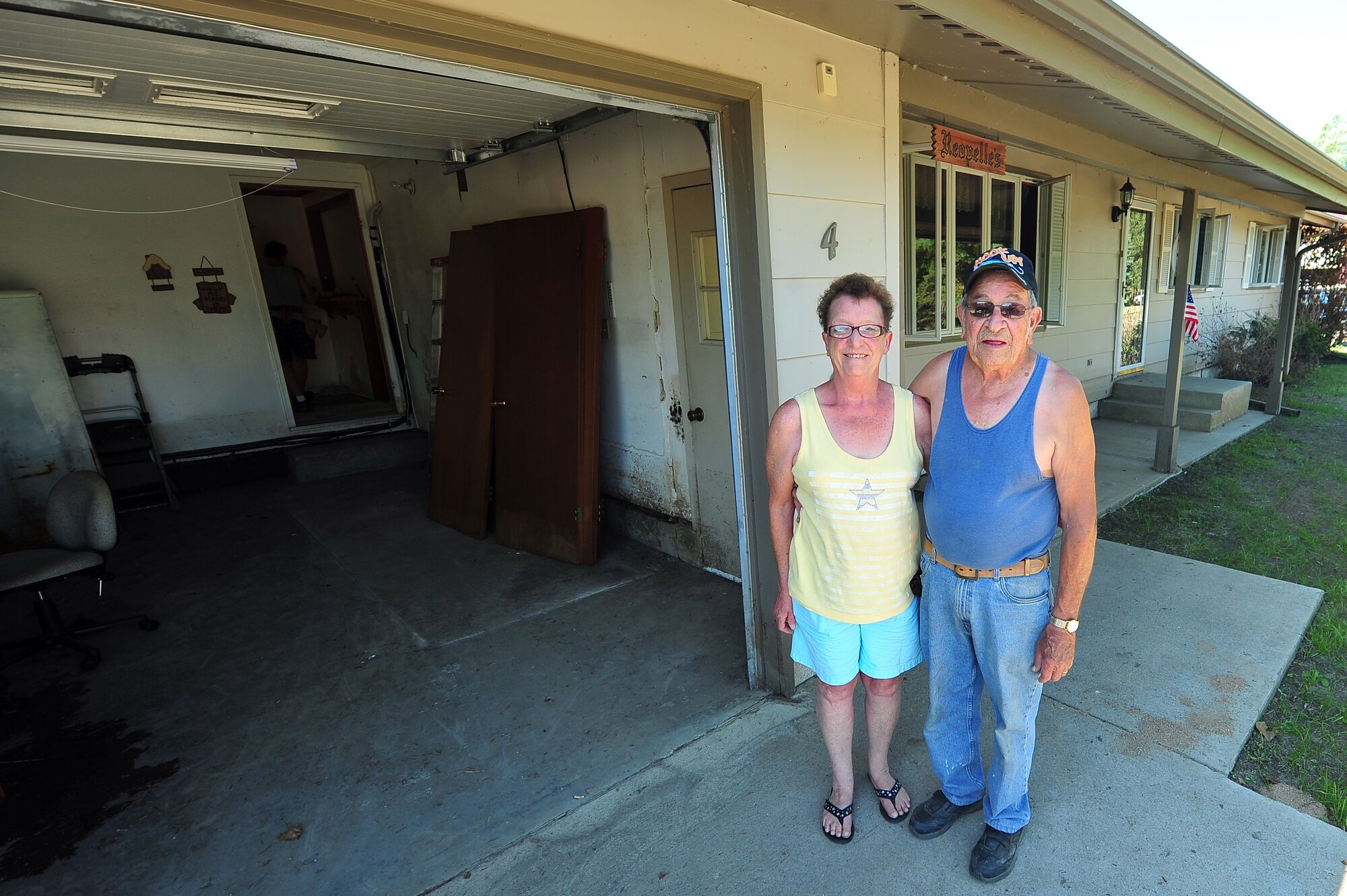 MINOT, N.D. – Vern and Idabel Reopelle, parents of Chief Master Sgt. Mechele Greene, an Air Force Intelligence, Surveillance and Reconnaissance superintendent at the Pentagon, stand in front of their damaged home as they begin to remove flooring and drywall here, July 22. With Greene having had major hip replacement surgery, Airmen from Minot Air Force Base helped her parents with the recovery efforts. (U.S. Air Force photo/ Senior Airman Jesse Lopez)