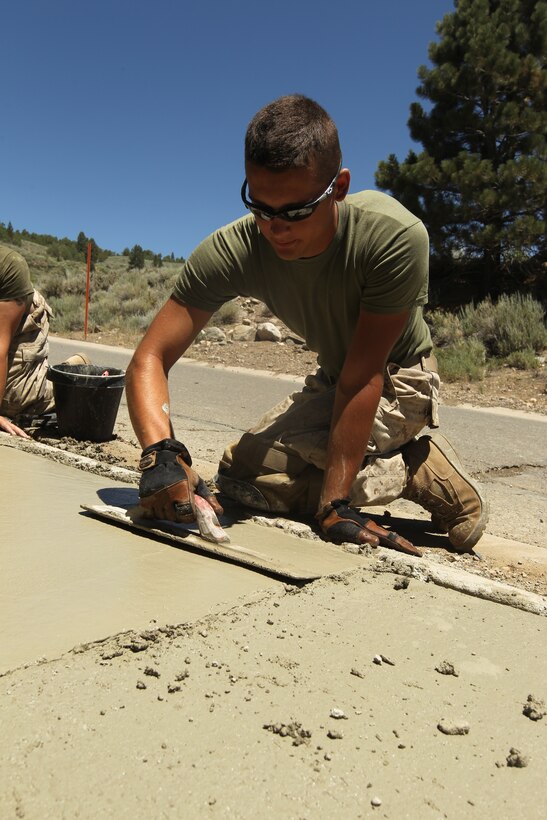 Lance Cpl. Joseph W. Landes, a combat engineer with Company C., 3rd Engineer Support Battalion and a Jacksonville, Ill., native, smooths out the finishing touches for a 500 foot sidewalk in support of the Marine Corps Mountain Warfare Training Center, July 26.