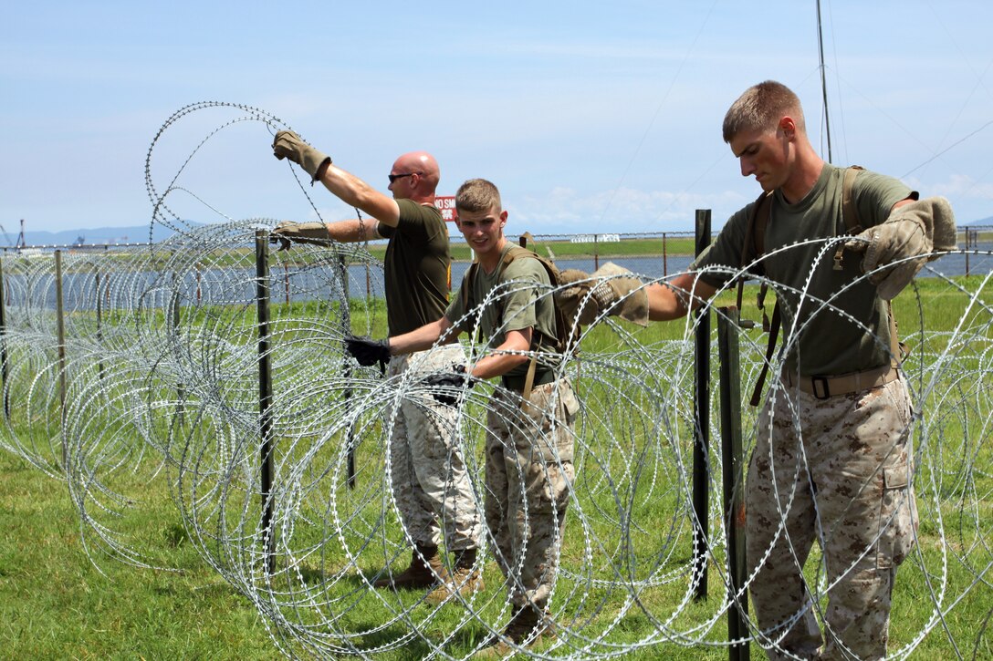 Sgt. Adam Smith, Pfc. Tyler Teigen, and Lance Cpl. David Waldbillig, MWSS-171 combat technicians set up concertina wire around the perimeter of the simulated combat operations center at Penny Lake here July 28. Combat engineers were called out during the first few days of the exercise to help set up the exterior.