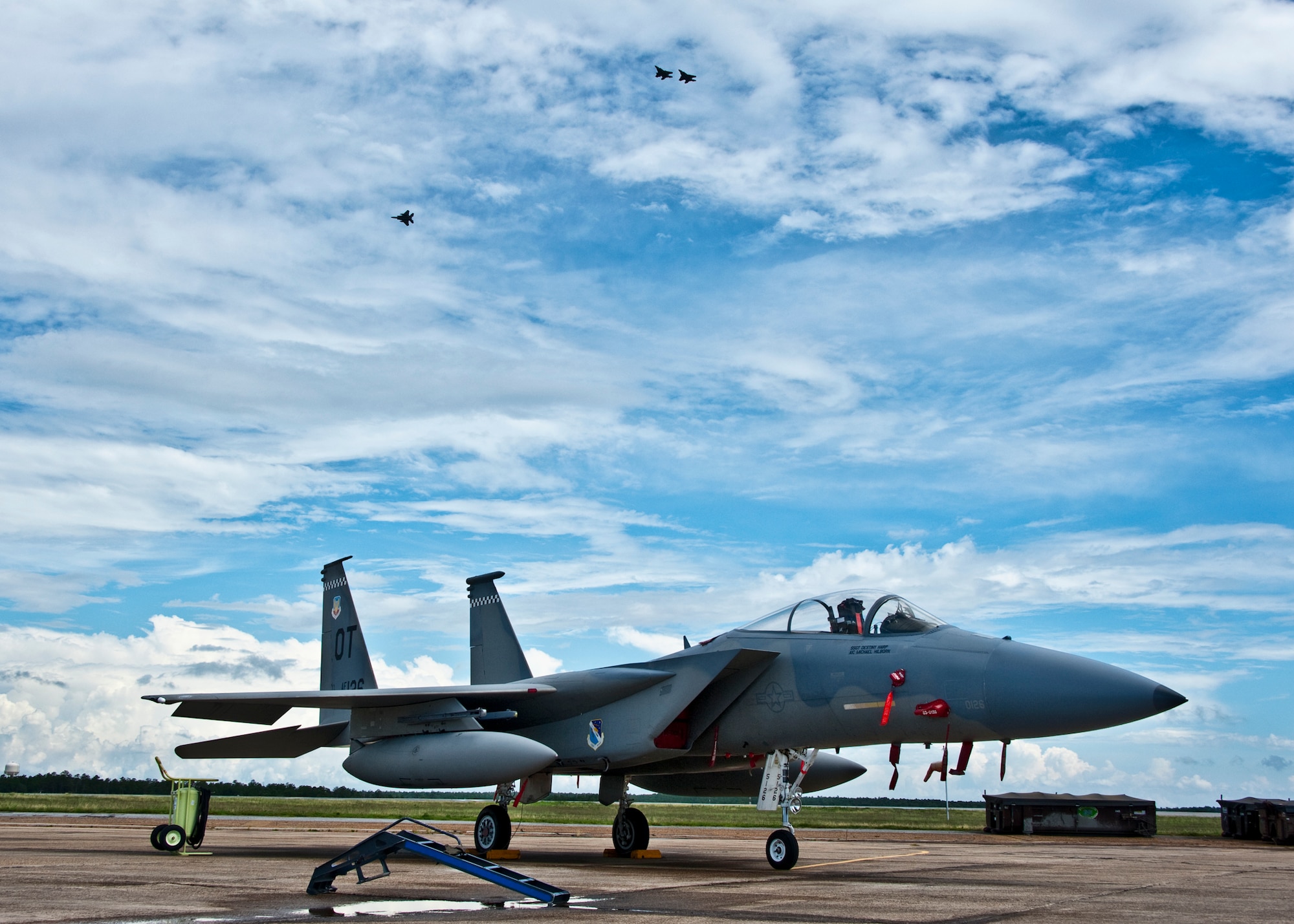 A 53rd Wing F-15 waits for its next mission as an F-15 and F-16s fly over the Eglin Air Force Base, Fla., runway July 22.  These and other aircraft share Eglin’s flightline and runways with the Northwest Florida Regional Airport.   (U.S. Air Force photo/Samuel King Jr.)
