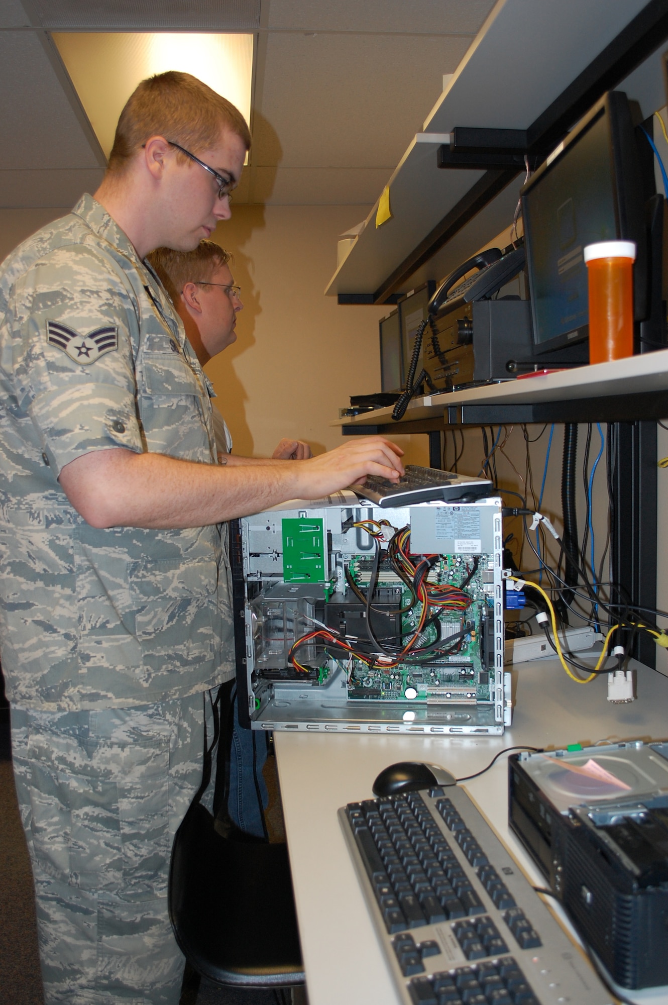 Senior Airman Michael Silva, 341st Communications Squadron Customer Support Technician, works to rebuild a customer's hard drive in preparation for the upcoming migration to the AFNet planned for early September. Assisting him in the background is Jesse Douglas, also a 341st CS/CST. (U.S. Air Force photo/Valerie Mullett)