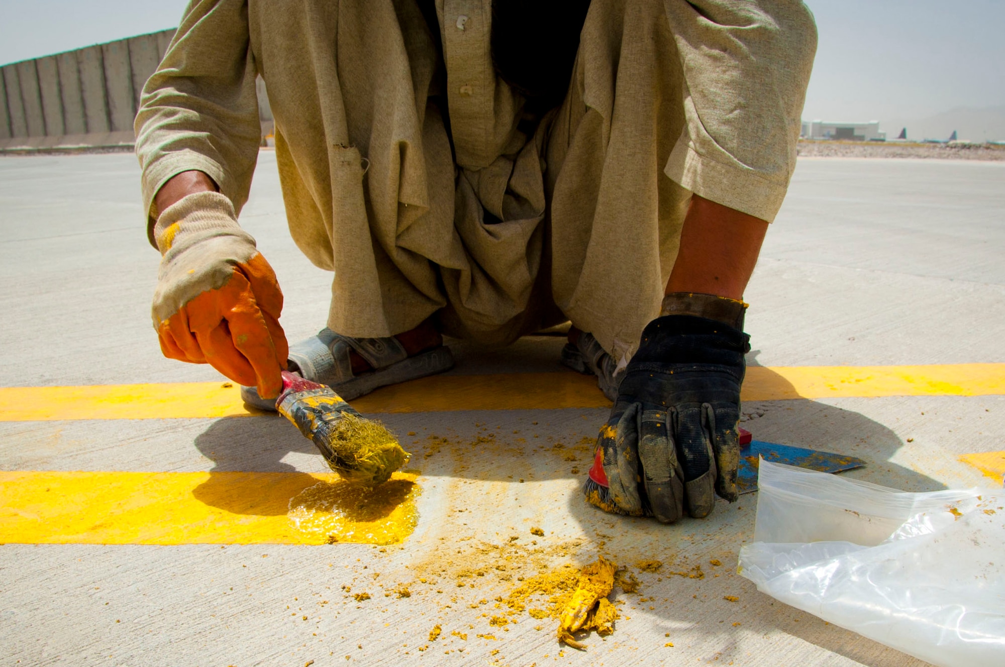 An Afghan worker applies a fresh paint job near the flightline at Kandahar Air Field, Afghanistan, July 28, 2011. Many Afghans work construction or maintenance jobs at Kandahar Airfield. (U.S. Air Force photo by Senior Airman Corey Hook)