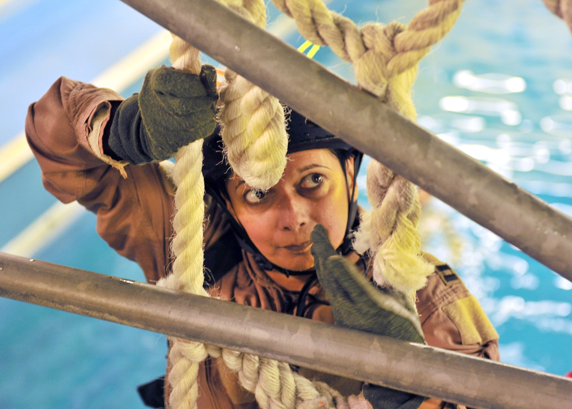 LOWESTOFT COLLEGE, England -- Karen Abeyasekere, 100th Air Refueling Wing Public Affairs, pulls herself up on the cargo net at the end of the water survival portion of survival, evasion, resistance and escape training July 14, 2011. The half-Olympic size pool is 16-feet deep, with pumps which create six- to eight-foot waves, fans which produce a 30-knot wind, and sprinkler system and lighting control to replicate horrific sea condtions. Abeyasekere, along with 12 U.S. Air Force members from RAFs Mildenhall and Lakenheath, underwent the training which included pulling yourself along underneath a parchute which lays on the water, and climbing into a life raft in severe storm conditions and in complete darkness. (U.S. Air Force photo/Staff Sgt. Tabitha Lee)