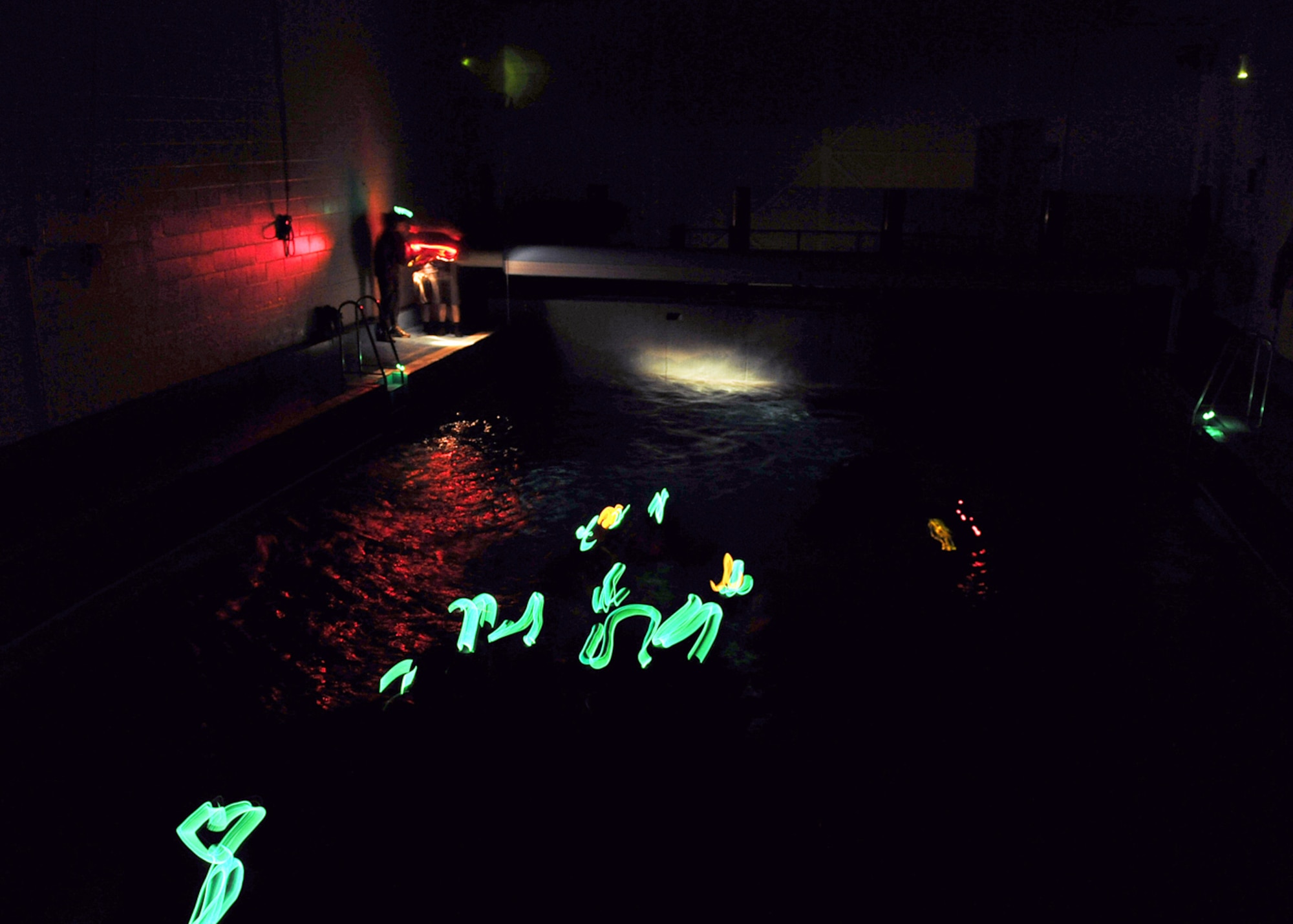 LOWESTOFT COLLEGE, England -- The fluorescent light from glow sticks fastened on helmets, the beam from a small flashlight is all that can be seen as the pool at Lowestoft College is switched to stormy, night-time conditions during the water survival portion of survival, evasion, resistance and escape training July 14, 2011. As part of the training, aircrew from RAFs Mildenhall and Lakenheath had to jump into the pool in almost complete darkness, with a wave machine creating six- to eight-foot waves, fans producing a 30-knot wind, and sprinkler system and lighting controls to replicate horrific sea conditions. Everyone had to form a chain, then swim to the life raft before climbing in and pulling the cover over the top -- with each person holding it down and over the sides, in an attempt to stop water pouring in. The SERE instructors teach this training every month, holding twelve training sessions per year. (U.S. Air Force photo/Staff Sgt. Tabitha Lee)
