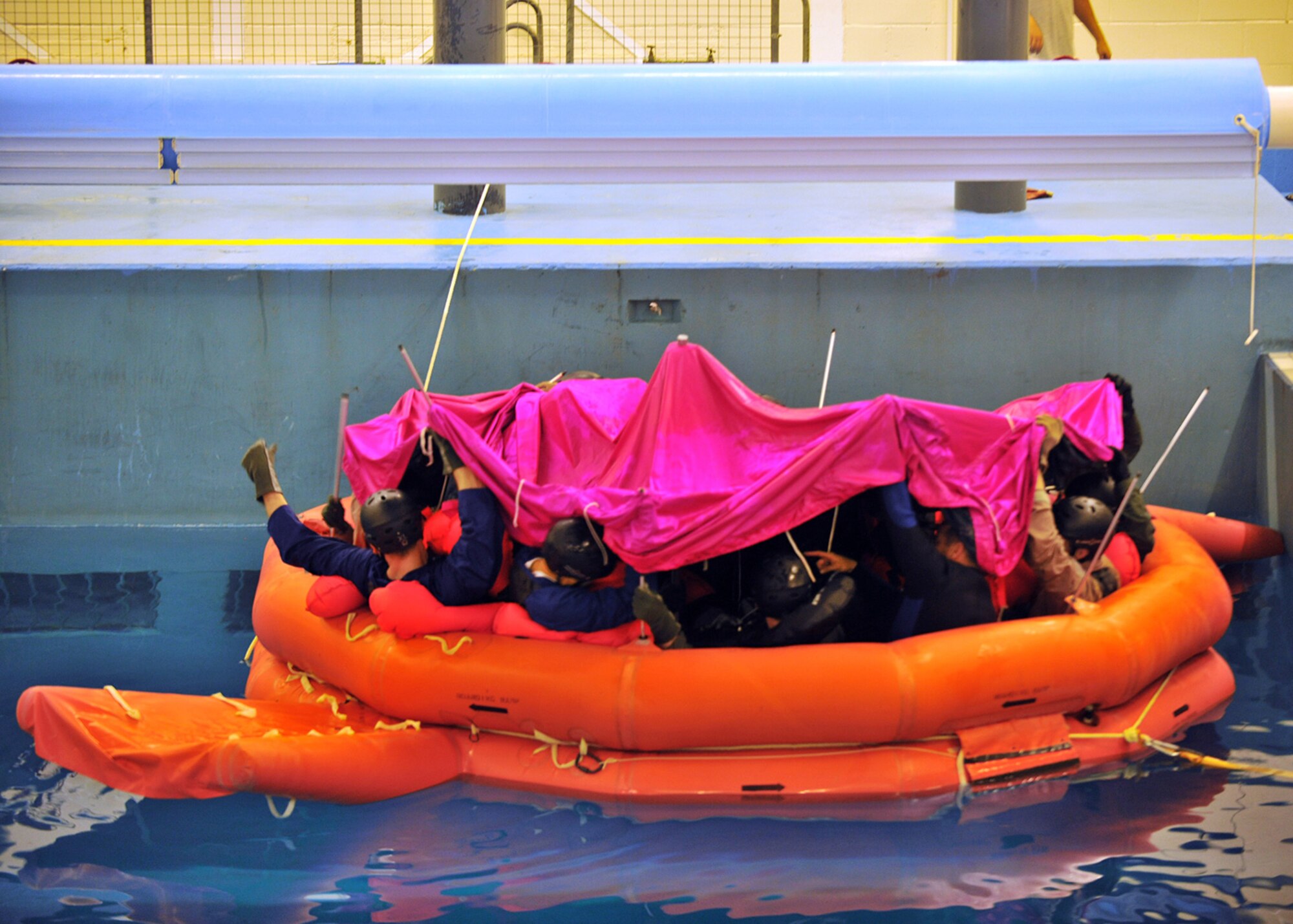 LOWESTOFT COLLEGE, England -- Aircrew members from RAFs Mildenhall and Lakenheath pull the cover of a life raft over their heads as a survival, evasion, resistance and escape instructor explains how to use special poles to position it properly July 14, 2011. The cover is neon-bright so as to be seen from the air to aid in rescue. (U.S. Air Force photo/Staff Sgt. Tabitha Lee)