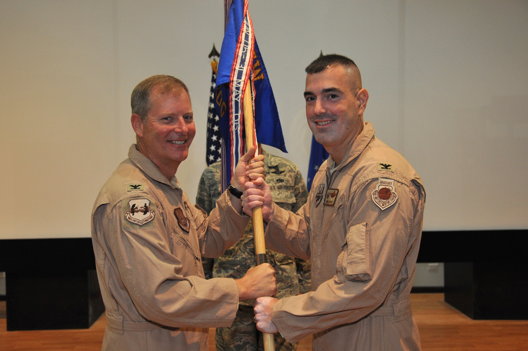 Col. Michael Zick, 386th Air Expeditionary Wing commander, left, passes the 386th Expeditionary Operations Group guide-on to Col. Mark August during a change of command ceremony July 29 at an undisclosed location in Southwest Asia. Colonel August assumed command of the 386th EOG from Col. Scott Brewer.  (U.S. Air Force photo by Master Sgt. Carlotta Holley)