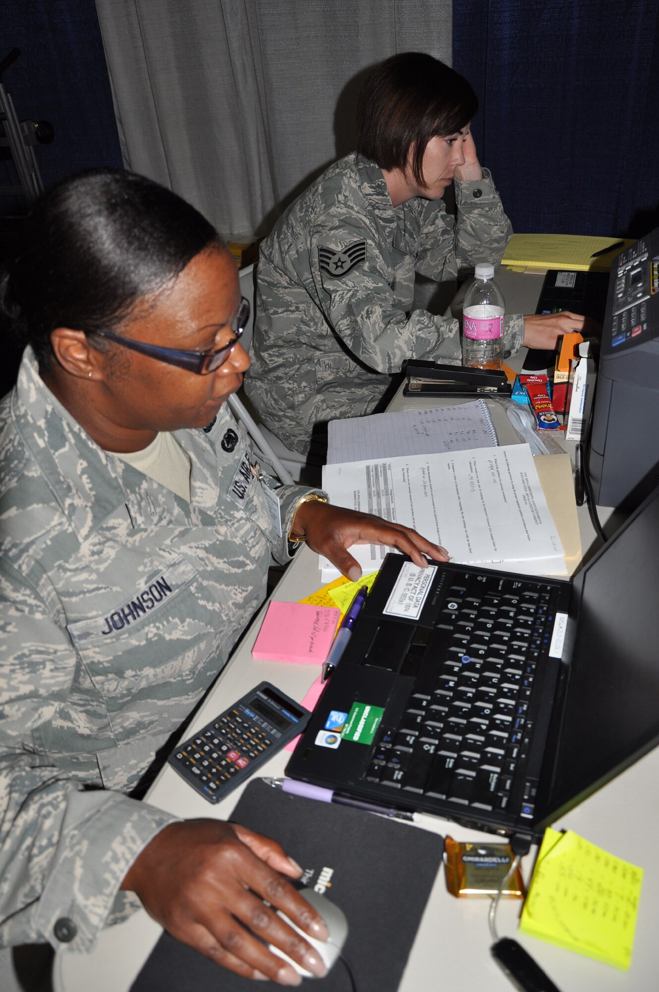 From front, Tech. Sgt. Adrienne Johnson and  Staff Sgt. Christie Bates, 92nd Comptroller Squadron, work in their simulated deployed environment behind curtains in Joint Base Lewis-McChord's Hangar 2, Wash., July 28 as part of the Air Mobility Rodeo. The finance specialists worked 155 scenarios in four days as part of their competition. (U.S. Air Force Photo/Tech. Sgt. Jennifer Buzanowski)