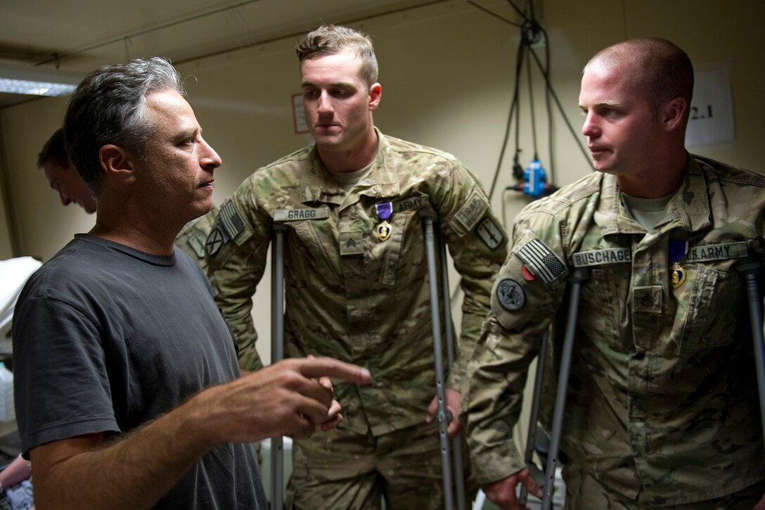 Comedian Jon Stewart visits with Army Sgt. Jason Gregg, left, and Staff Sgt. Matthew Buschagen, right, at Tarin Kowt Hospital in Afghanistan, July 30, 2011. Gregg and Buschagen were presnted the Purple Heart by U.S. Navy Adm. Mike Mullen, chairman of the Joint Chiefs of Staff, for injuries sustained during action. 