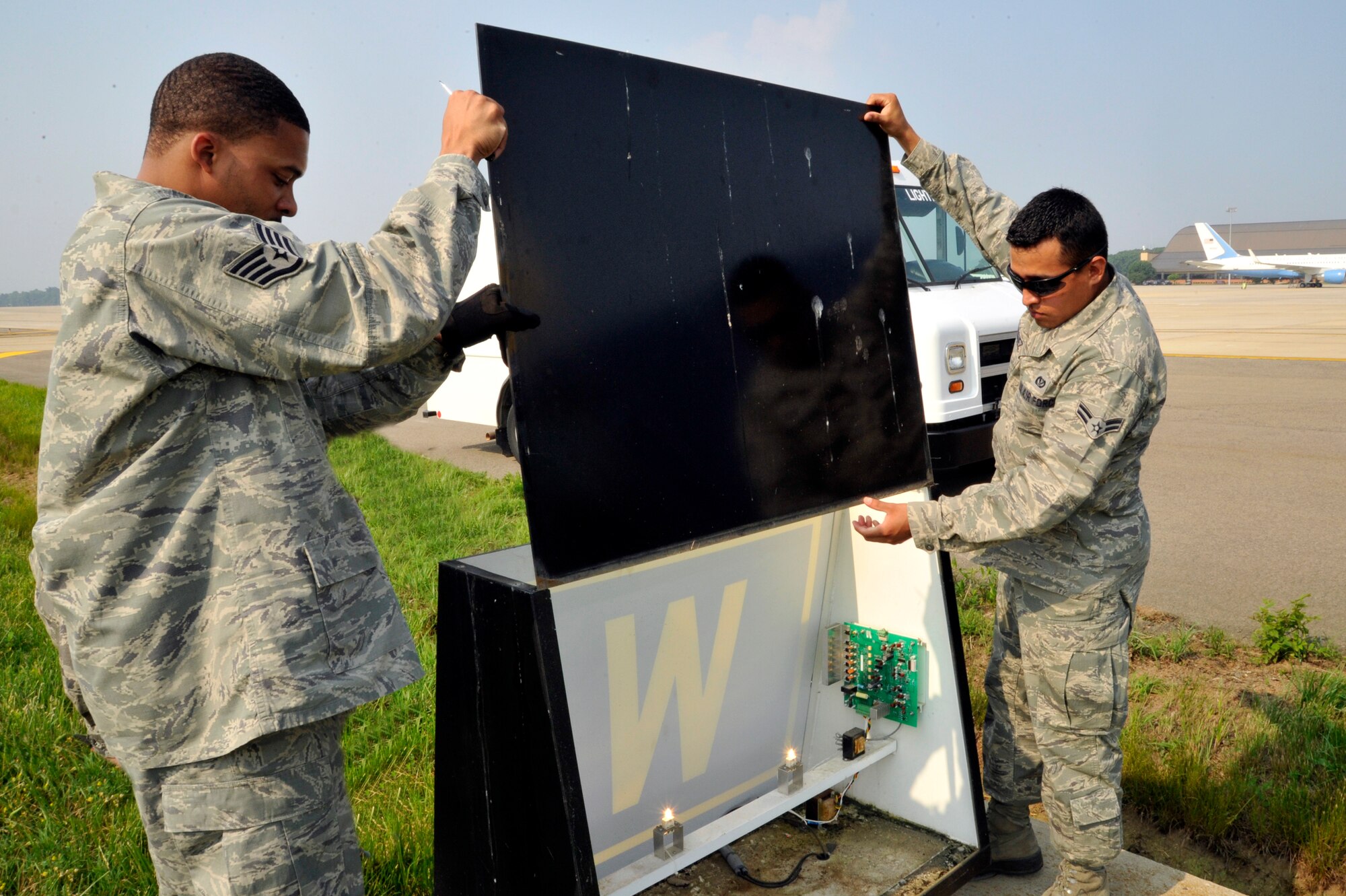 Staff Sgt. Brian Myers Jr., 11th Civil Engineer Squadron airfield lighting NCO in charge, and Airman 1st Class Erick Rodriguez, 11th CES electrical systems apprentice, replace the case of a taxiway location sign after replacing the lights and adjusting the brightness June 1, 2011 at Joint Base Andrews, Md. The Airmen of 11th CES airfield lighting maintain all the lights and their electrical systems on the flightline. (U.S. Air Force photo/Senior Airman Perry Aston)