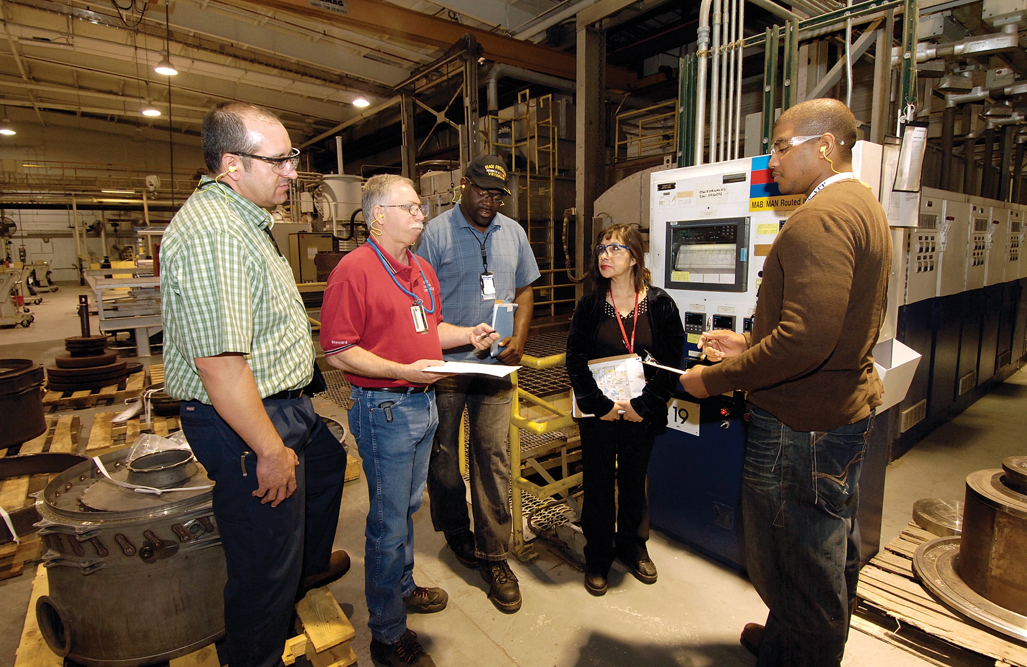 A group of 76th Maintenance Support Group members committed to employee safety through the Voluntary Protection Program regularly walk through MXSG shops and buildings, ensuring workers are protected and safety issues are addressed.  From left, Garrick Mickelson, Dennis Case, Theodore McNeal, Magaly Roberson and Justin Norman discuss lock out/tag out stickers and forms for Bldg. 3001’s Heat Treat furnace.  The forms and stickers alert whether electricity is flowing to the high-voltage equipment and can protect workers from serious injury or death. (Air Force photo by Margo Wright)