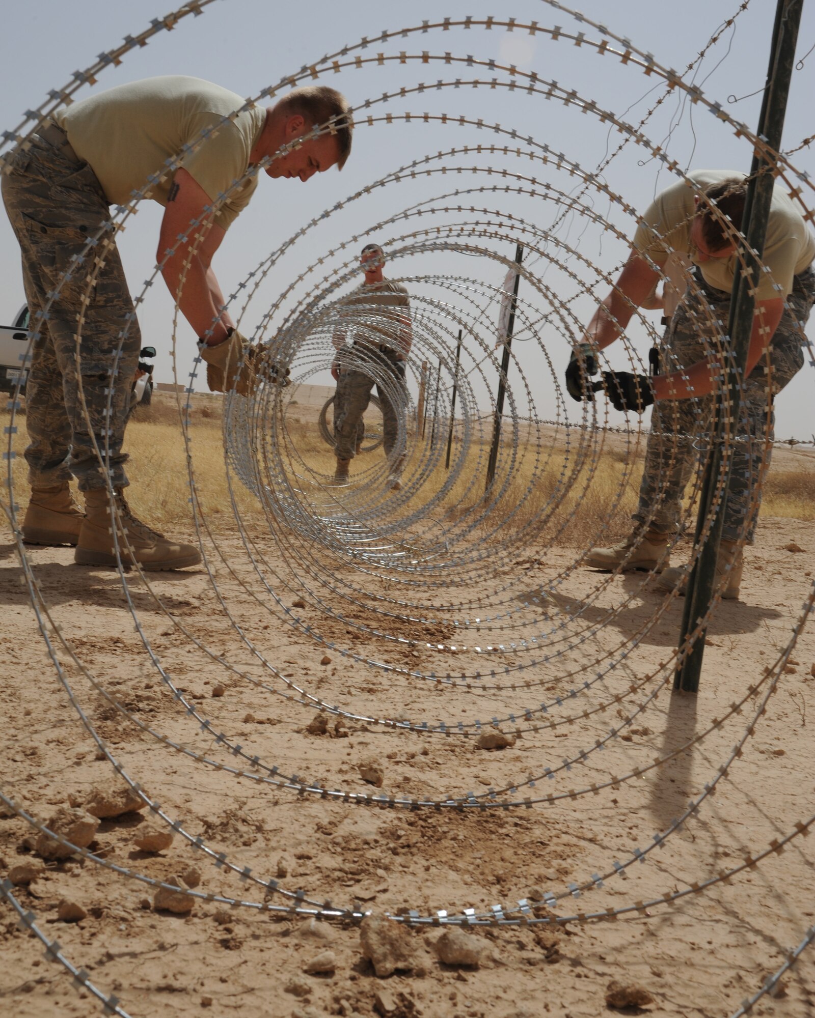 U.S. Air Force Airmen 1st Class Denton Weimer, left, Christopher Rodacker, background, and Ethan Olson, right, 532nd Expeditionary Operations Support Squadron security forces flight, set concertina wire May 27, 2011, at Al Asad Air Base, Iraq. Airmen at the remote, desert runway in western Al Anbar Province regularly work outside in 125 degree temperatures. (U.S. Air Force photo by Senior Airman Tristin English)