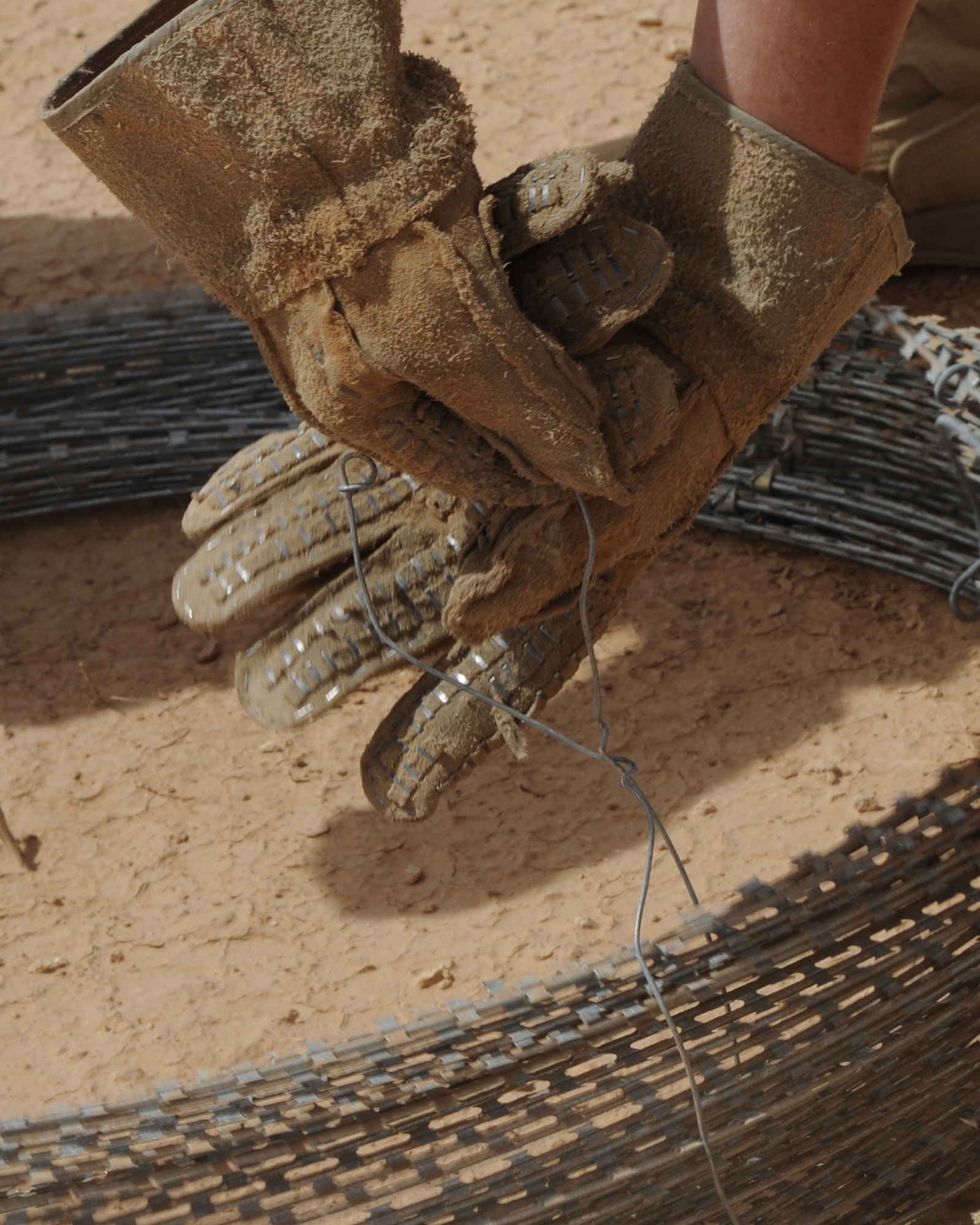 An Airman begins to unwind ties in order to uncoil concertina wire May 27, 2011, at Al Asad Air Base, Iraq. Airmen from the 532nd Expeditionary Operations Support Squadron security forces flight have placed 18 miles of wire around the 13,000 feet long runway to improve force protection of aircraft, equipment and personnel. (U.S. Air Force photo by Senior Airman Tristin English)