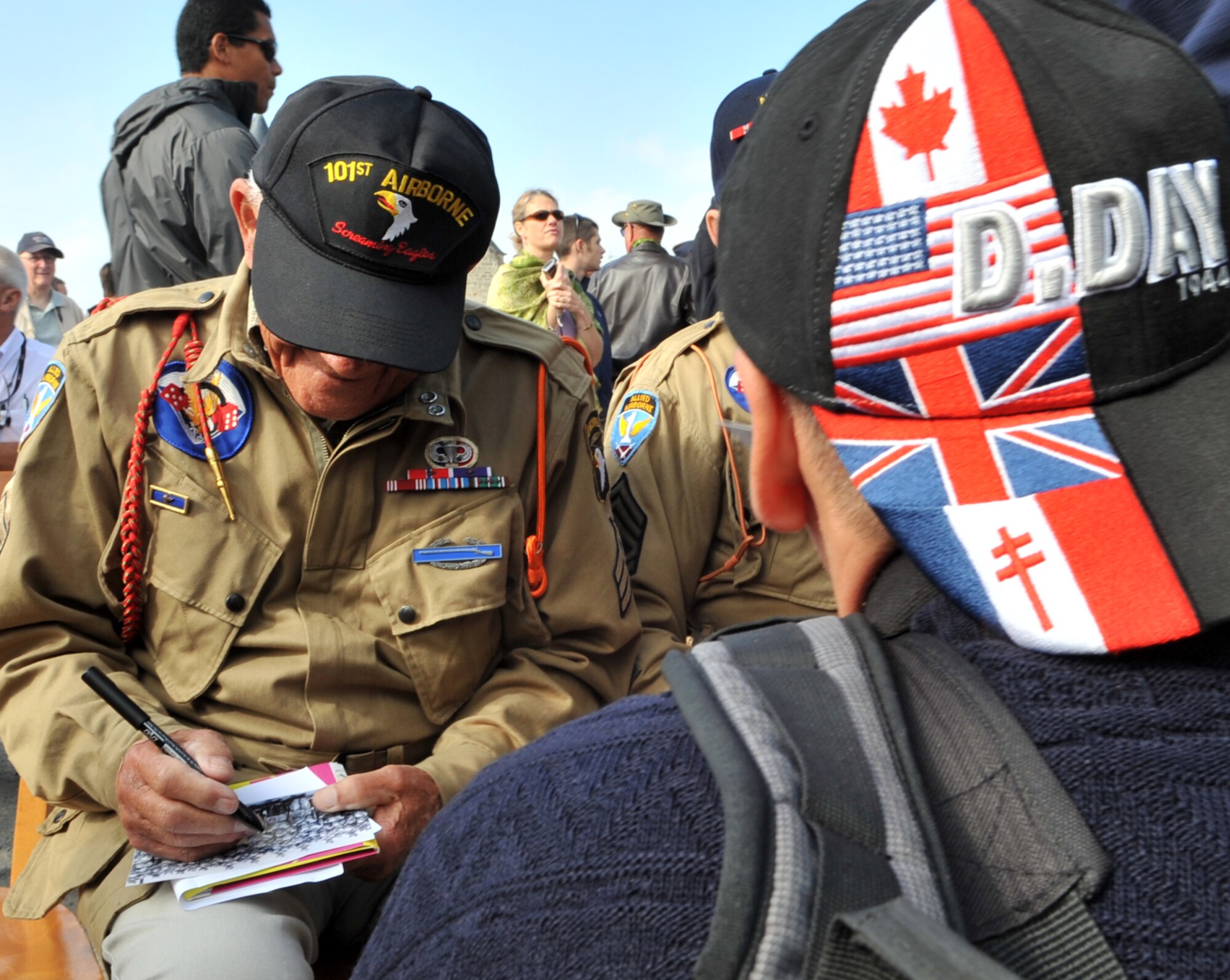 A World War II veteran signs memorabilia for those in attendance at a ceremony in Picauville, France for the 67th Anniversary of D-Day, June 3, 2011. Each year since the liberation of Normandy, U.S. forces along with allied nations come together to honor those who gave the ultimate sacrifice on that day. This year's ceremony is scheduled to be attended by dozens of American World War II veterans. (U.S. Air Force photo by Senior Airman Caleb Pierce)