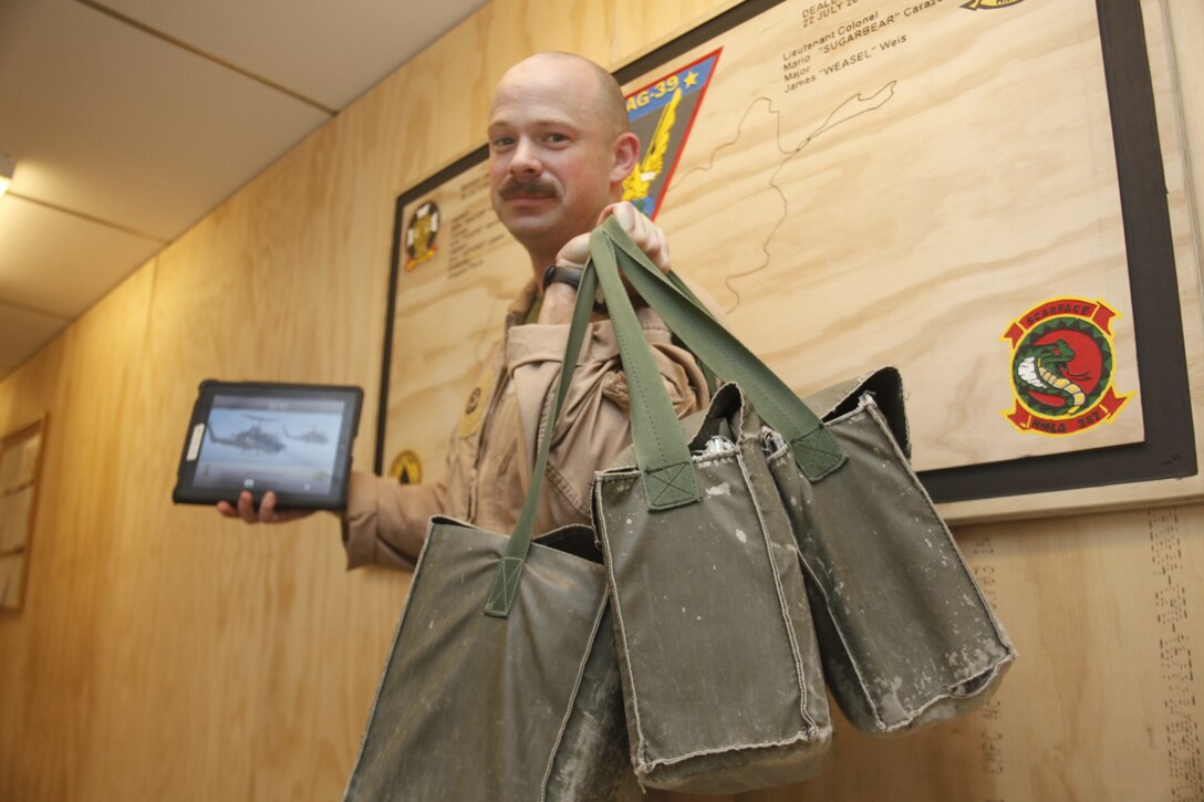 Maj. Brian Ashford displays the difference between pilots carrying their regularly issued map packs weighing in at nearly 40 pounds versus the 1.33-pound iPad, which holds the same amount of maps. AH-1W pilots have been using the iPad to quickly access maps and other data they can use to ensure precision strikes are targeted at enemy positions. Ashford is the operations officer for Marine Light Attack Helicopter Squadron 267.