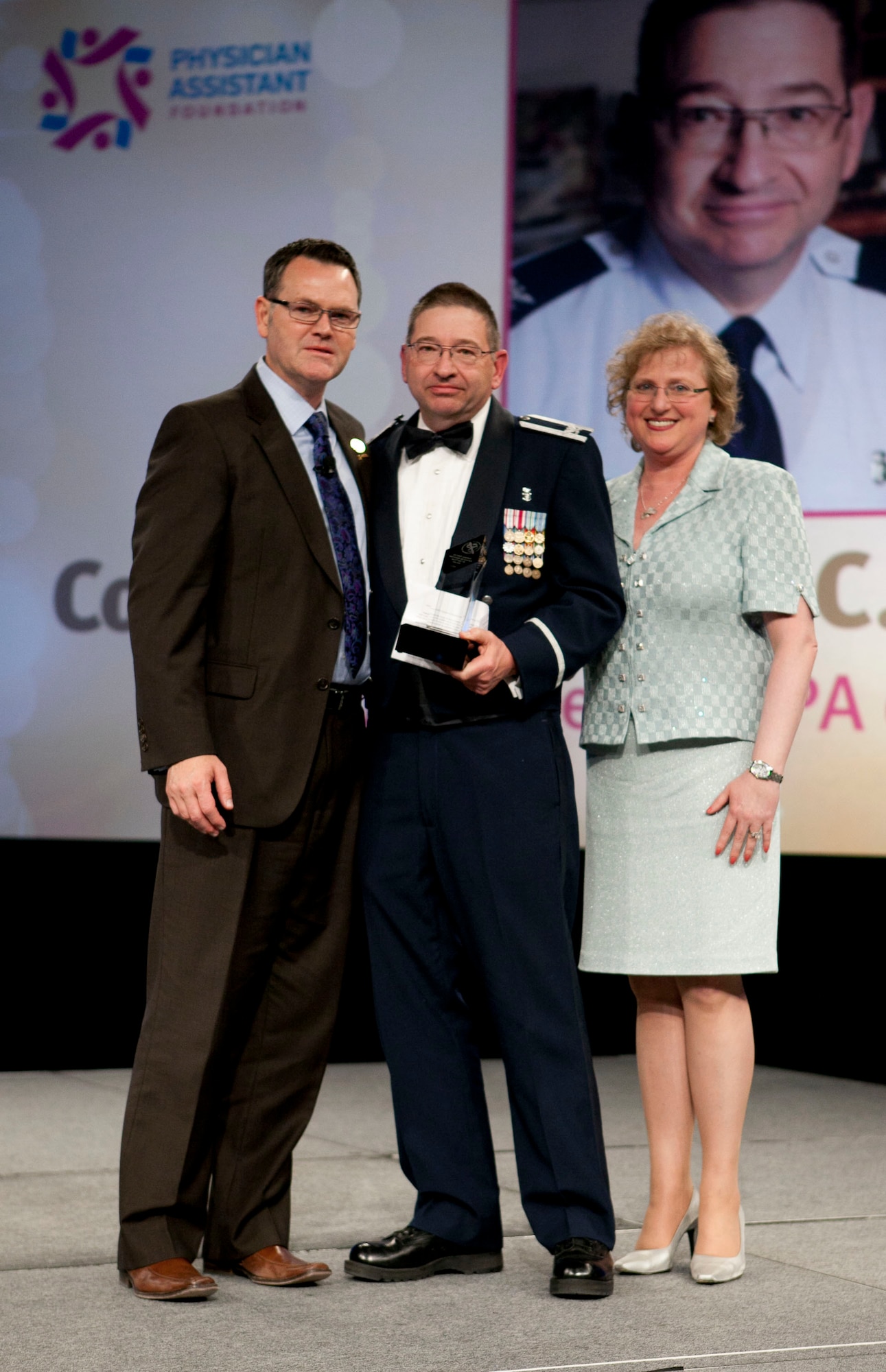 Colonel Douglas Hodge (center), Deputy Director of the Human Effectiveness Directorate, 711th Human Performance Wing, Air Force Research Laboratory at Wright-Patterson Air Force Base, Ohio, received the American Academy of Physician Assistants’ 2011 Federal Service PA of the Year Award at the organization’s conference on June 1 in Las Vegas. Patrick Killeen (left), President, American Academy of Physician Assistants, and Dr. Roslyn Schneider (right), Chief of Staff of the Medicines Development Group, Primary Care Business Unit, Pfizer Inc. and Physician Assistant Foundation trustee, present Colonel Hodge with his award.