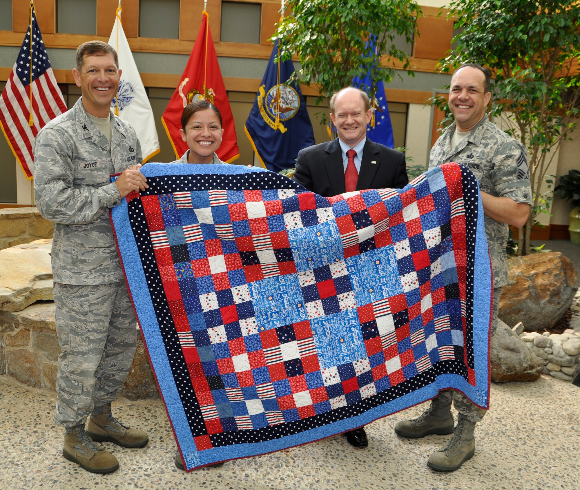 Col. Thomas C. Joyce, (left) Air Force Mortuary Affairs Operations commander, presents Senior Airman Dayra Rodriguez Rodriguez, a Quilt of Valor with the help of Sen. Chris Coons of Delaware and Chief Master Sgt. David Fish, AFMAO chief enlisted manager. Airman Rodriguez Rodriguez is an X-ray technician deployed to the Charles C. Carson Center for Mortuary Affairs from Lackland Air Force Base, Texas. She is completing a 6-month rotation. The senator paid a visit to the mortuary to thank the men and women for the work they do in honoring America's fallen heroes. He compared the symbolism of the quilts pieced together to the team at the mortuary, explaining how although they may vary in age, ethnicity,  branch of service and may come from different parts of the country, they all work together professionally to provide dignity to those who have made the ultimate sacrifice. Quilts have been long-standing American tradition during times of war. The quilts are made from volunteers for the Quilts of Valor Foundation whose mission is to provide quilts to individuals who have been wounded or touched by war. (U.S. Air Force photo/Tech. Sgt. Michael Stewart)