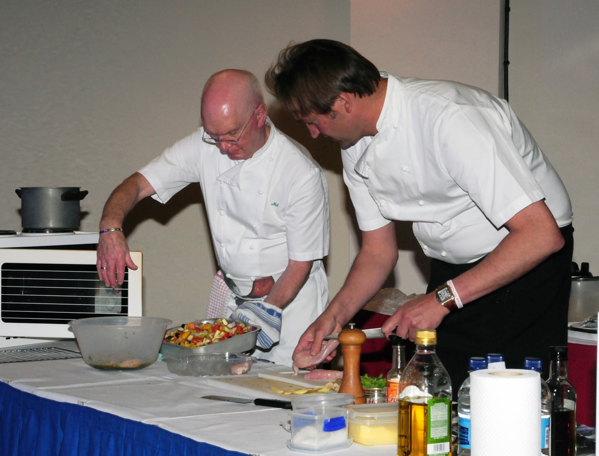 RAF MILDENHALL, England -- British celebrity chef, Galton Blackiston, right, prepares chicken for his 'Oriental-style chicken' dish, to serve with 'Rustic Ratatouille', held by his assistant, Neil Alston, during a cooking demonstration at the Galaxy Club June 9, 2011. Chef Blackiston has been on various British television cooking programs, published several books, and owns a hotel restaurant in Norfolk. During his visit, he demonstrated preparing and cooking some of his dishes, which are healthy options for a healthier lifestyle. (U.S. Air Force photo/Karen Abeyasekere)