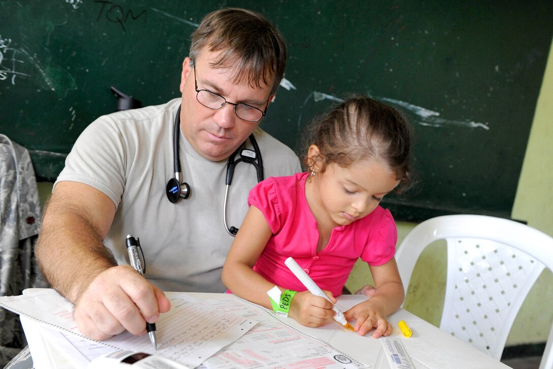 U.S. Air Force Maj. Gary Ruesch completes medical forms while his patient draws a picture at the Escuela Max Seidel medical site during Continuing Promise 2011 in Tumaco, Colombia, June 9, 2011. Ruesch is a nurse practitioner. Continuing Promise is a five-month humanitarian assistance mission to the Caribbean, Central and South America.