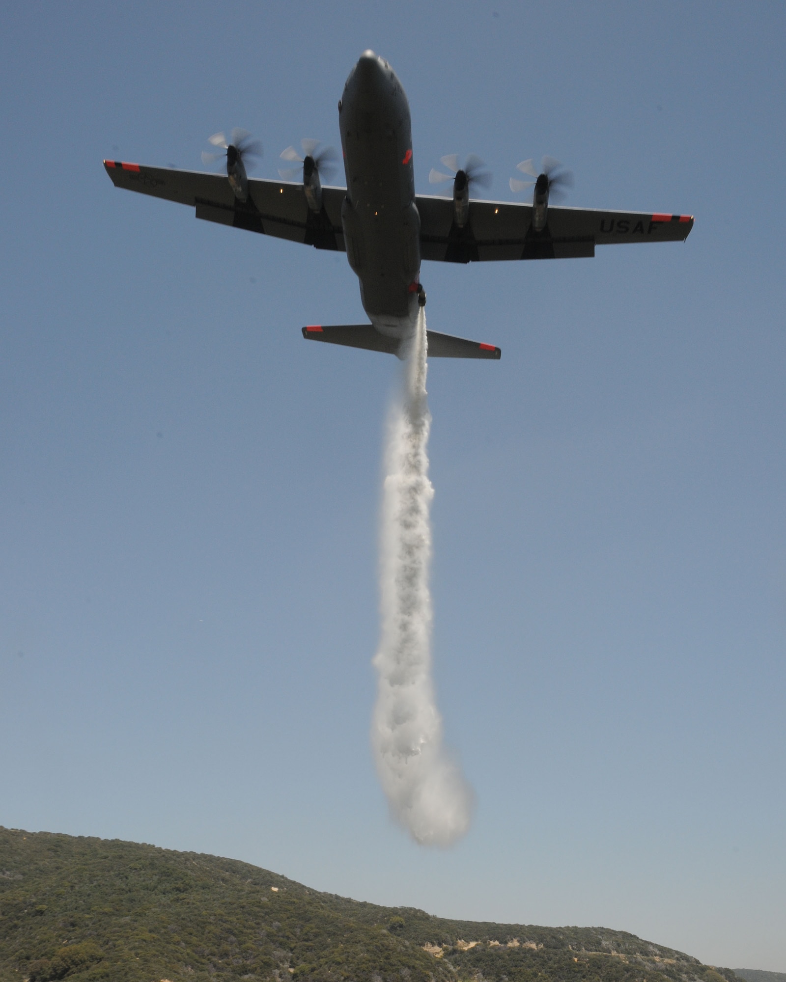 A C-130J from the 146th Airlift Wing, California Air National Guard, drops water over the Angeles Forest during Modular Airborne Firefighting System (MAFFS) training held June 7, 2011. The aircrews follow a U.S. Forest Service lead plane and demonstrate proficiency by dropping over a designated area. (Photo by Master Sgt. Dave Buttner)