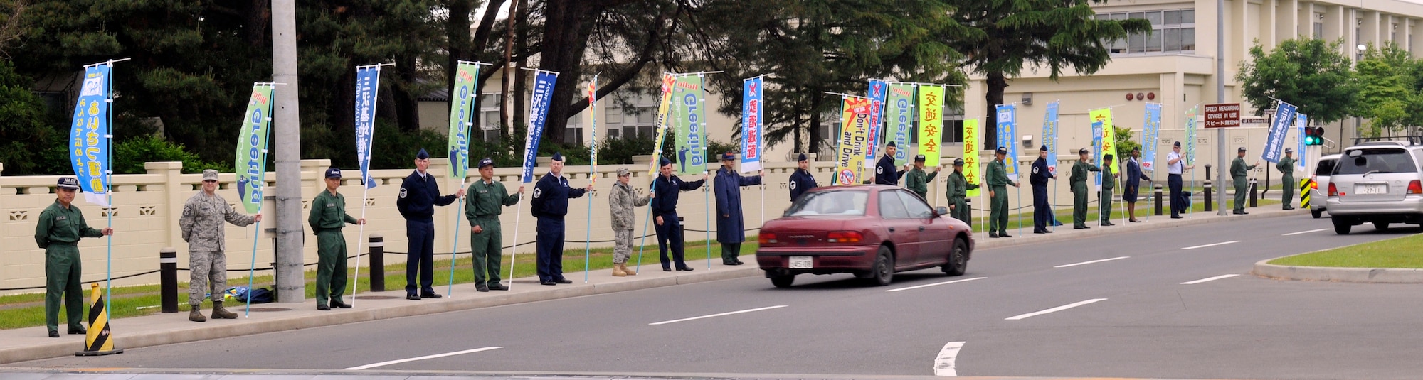 MISAWA AIR BASE, Japan— Members of Misawa’s Top 3 and the Japan Air Self-Defense Force Senior NCO Association hold flags, which display welcome and responsible driving messages in front of the main-gate 13 June. The Top 3 is a professional military organization, which strives to help senior NCOs progress through professional development as well as assist the on base and local community through mutually beneficial projects. (U.S. Air Force photo\Tech. Sgt. Phillip Butterfield) 