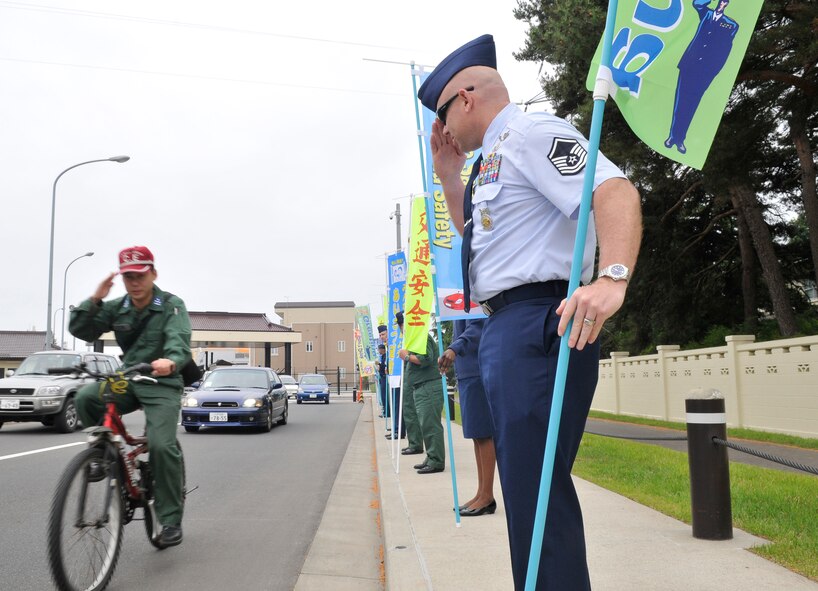 MISAWA AIR BASE, Japan— U.S. Air Force Master Sgt. Timothy Walsh, 35th Civil Engineer Squadron Fire Department training NCO in charge, salutes a Japan Air Self-Defense Force member as he rides past a procession of U.S. Air Force and JASDF senior NCOs June 13. Members of Misawa’s Top 3 and the JASDF Senior NCO Association teamed up at the main-gate to greet entrants and encourage safe driving. The senior NCOs held flags with messages of welcome and responsible driving written on them. (U.S. Air Force photo\Tech. Sgt. Phillip Butterfield) 