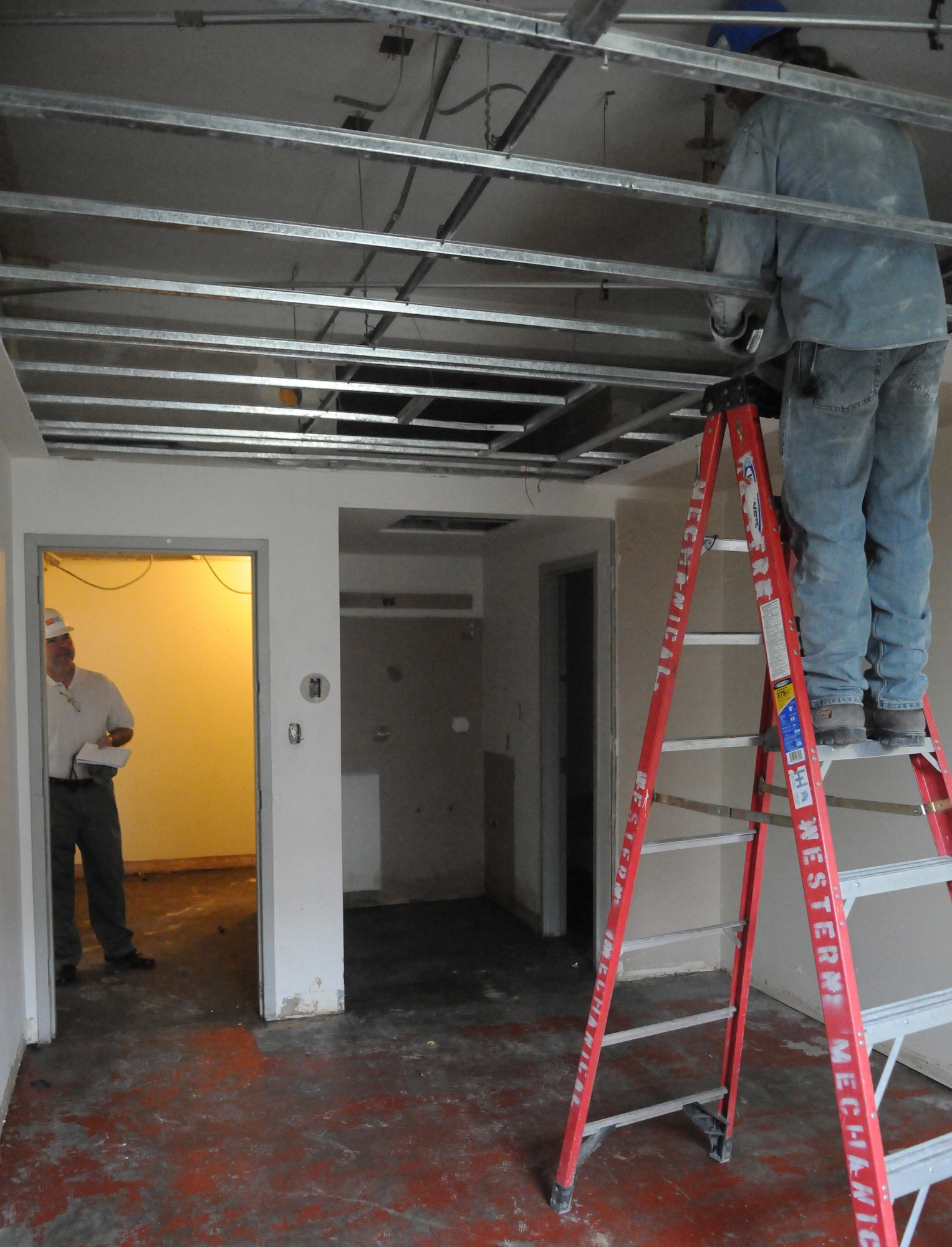A contractor performs construction in a dormitory room while John Moriarty looks on June 8, 2011, Eielson Air Force Base, Alaska. Two dormitories will receive construction, giving the inside a more updated look and more durable interior. John Moriarty is a 354th Civil Engineer Squadron project engineer. (U.S. Air Force photo/ Airman 1st Class Janine Thibault)