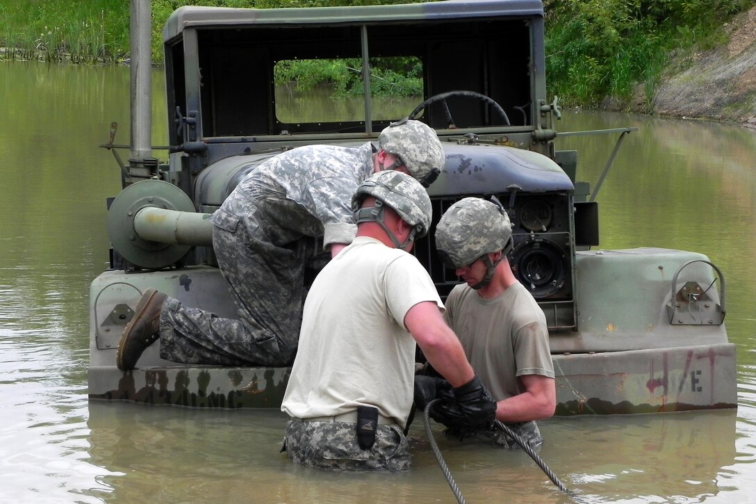 Army Staff Sgt. Keith Ericson, left, and Sgt. Ryan Johnson, right, wade in the water as they attach riggings to a mired multipurpose vehicle with the help of Spc. Andrew Miller during vehicle recovery training at Camp Ripley, Minn., June 8, 2011. Ericson is the vehicle recovery squad leader for the Headquarters Support Company, 834th Aviation Support Battalion. Johnson and Miller are mechanics with Headquarters Support Company, 834th Aviation Support Battalion.