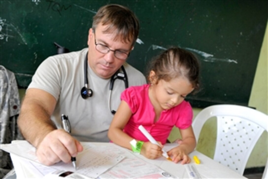 U.S. Air Force Maj. Gary Ruesch completes medical forms while his patient draws a picture at the Escuela Max Seidel medical site during Continuing Promise 2011 in Tumaco, Colombia, on June 9, 2011.  Ruesch is a nurse practitioner.  Continuing Promise is a five-month humanitarian assistance mission to the Caribbean, Central and South America.  
